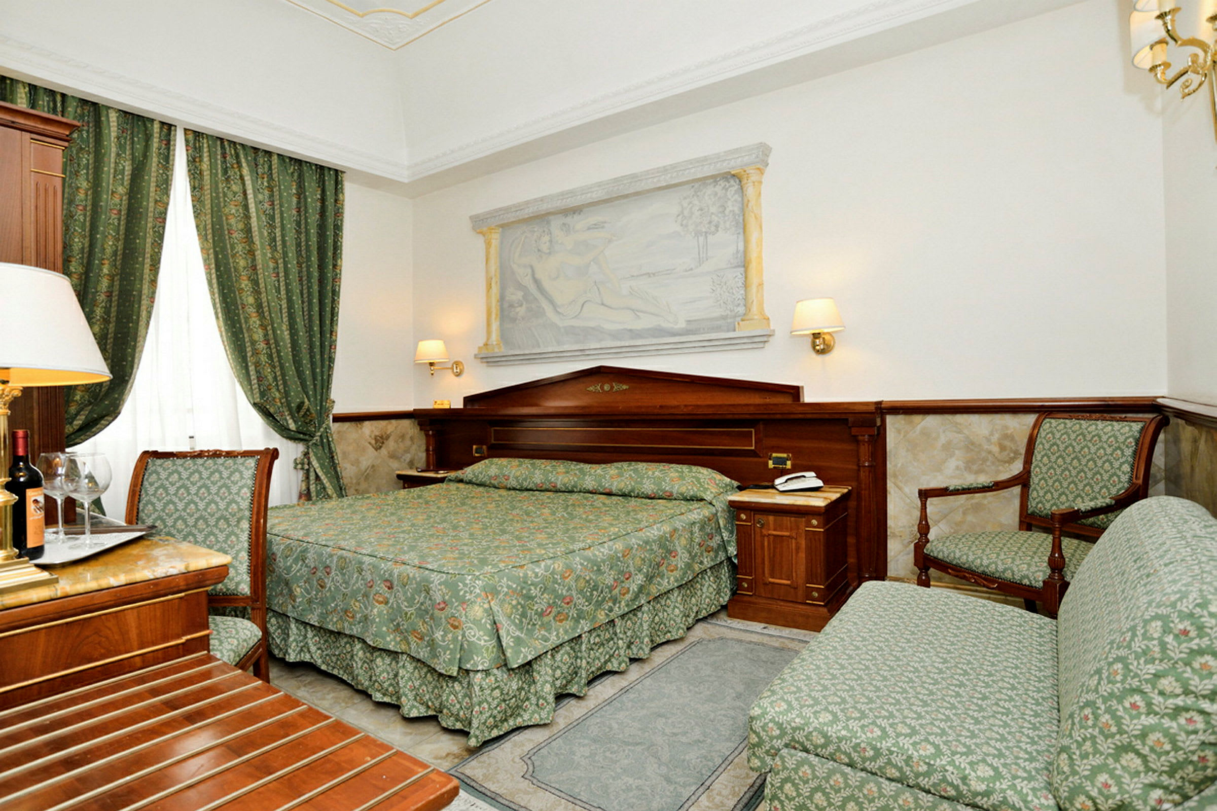 Hotellrum med grön inredning och trädetaljer, utrustat med en dubbelsäng, fåtölj och en soffa. (AI-genererad text)