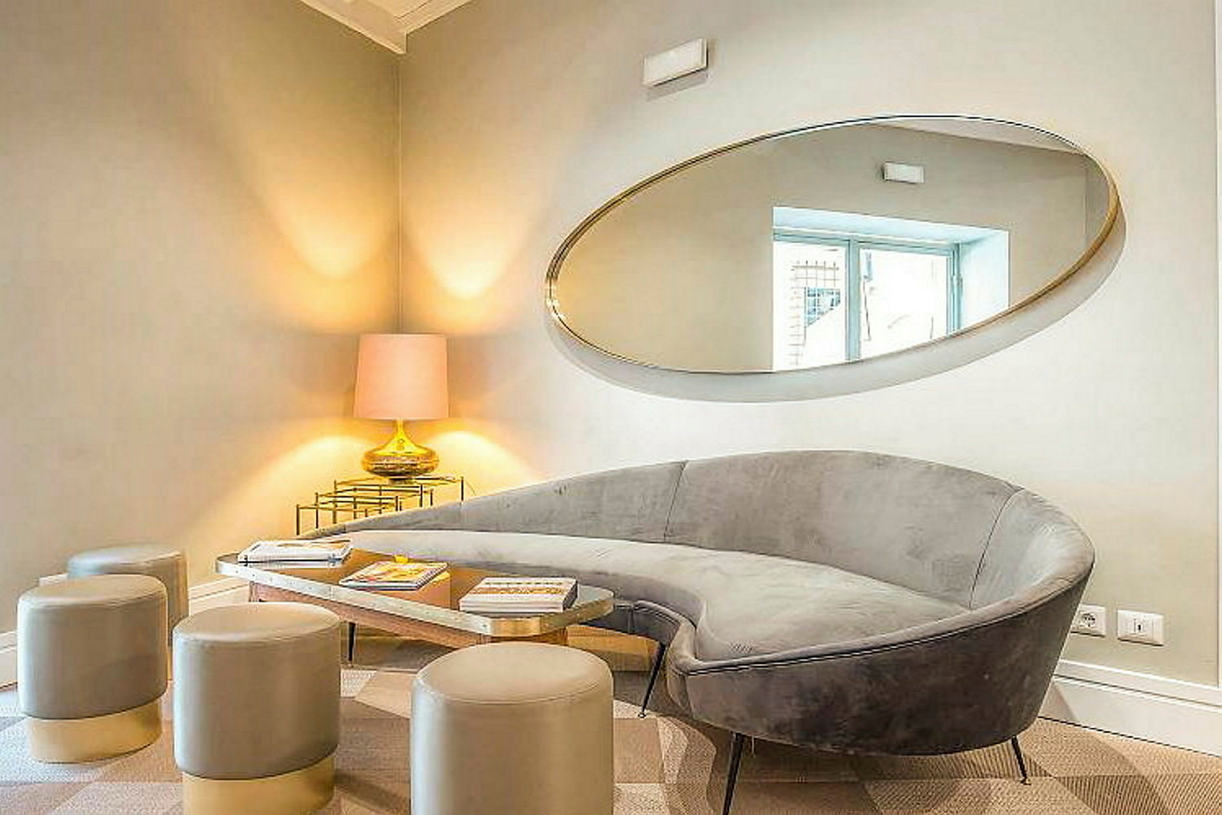 Ett elegant vardagsrum med en grå soffa, moderna sittpallar, ett speglat bord och en bordslampa placerad i hörnet. (AI-genererad text)