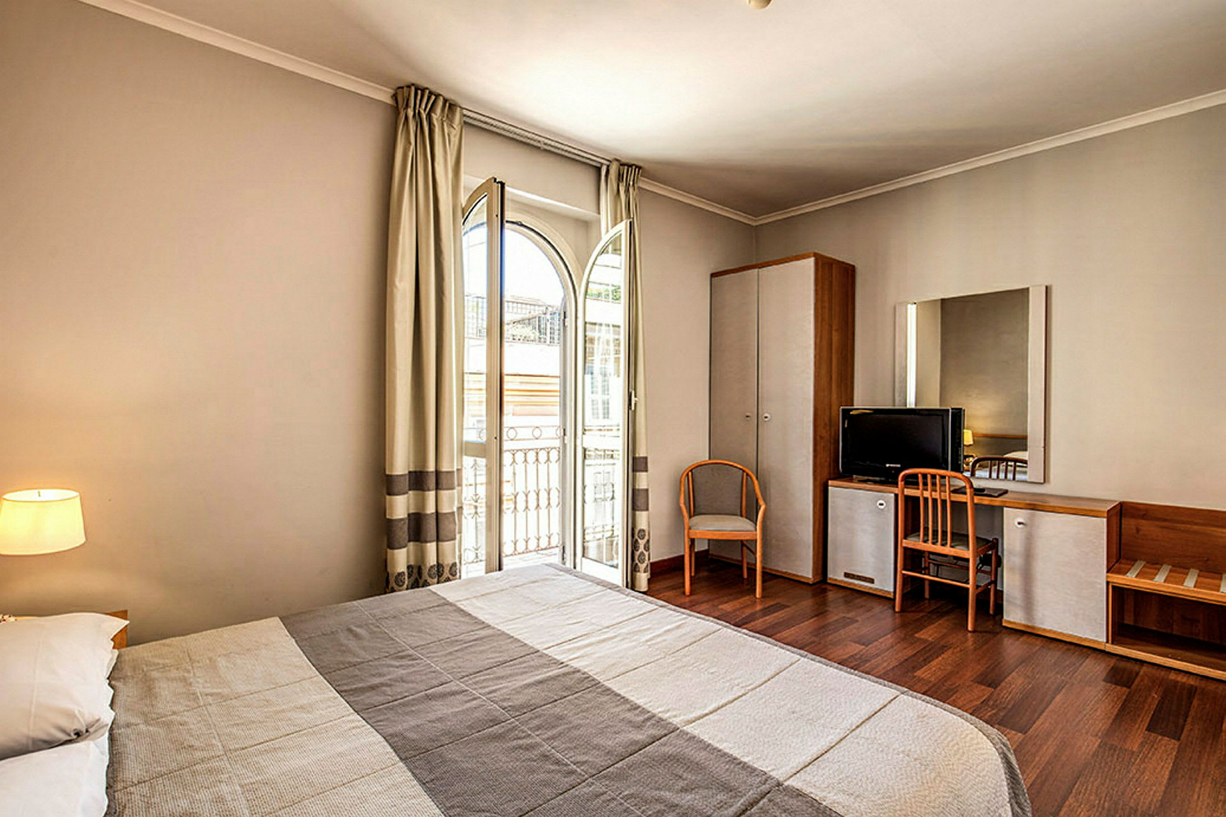 En bild av ett hotellrum med en säng, skrivbord, stol och ett öppet fönster. (AI-genererad text)