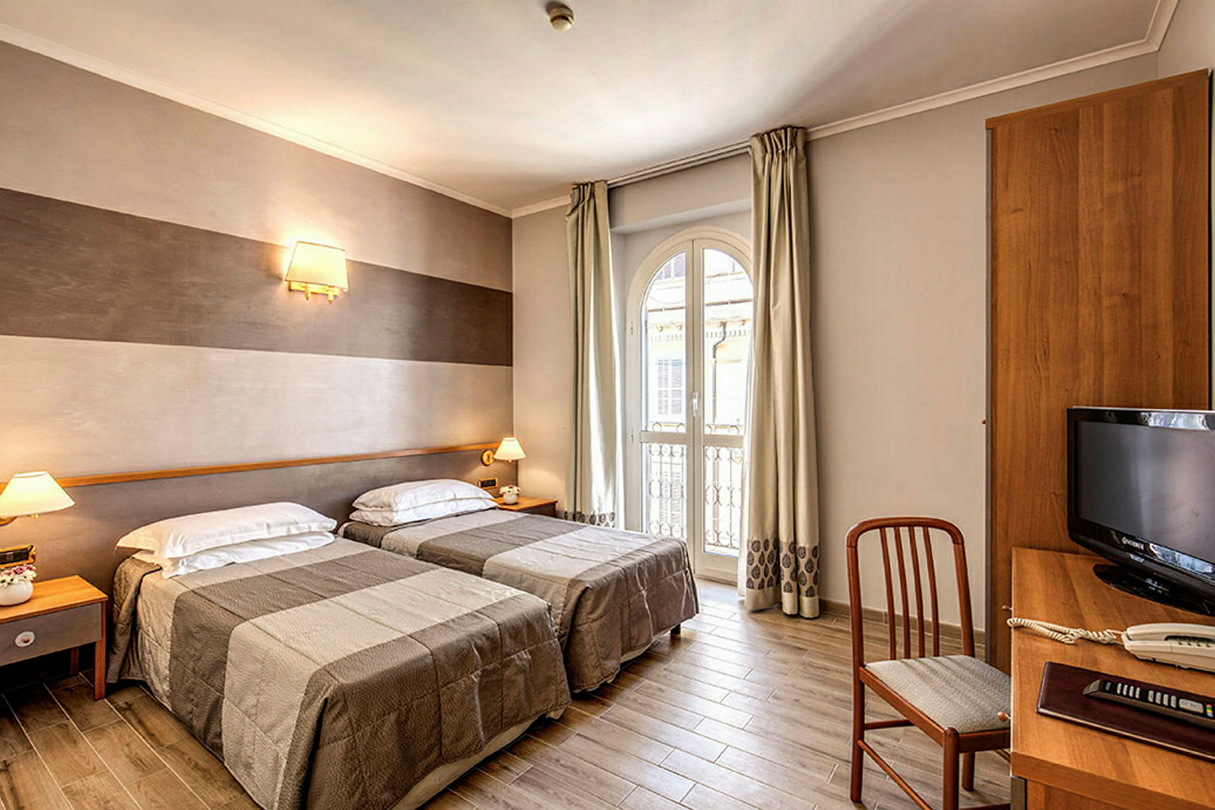 Ett hotellrum med två enkelsängar, en skrivbordshörna och ett stort fönster som släpper in dagsljus. (AI-genererad text)