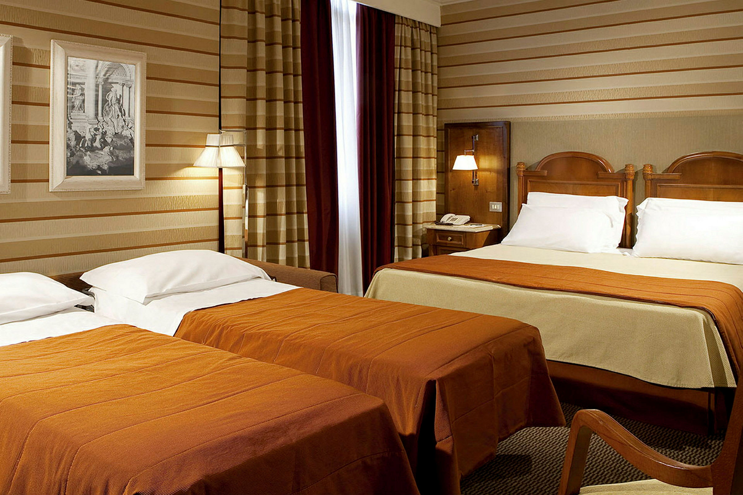 Ett hotellrum med två sängar, varav den ena är dubbelsäng. Sängarna har orange sängöverkast och vita kuddar. (AI-genererad text)