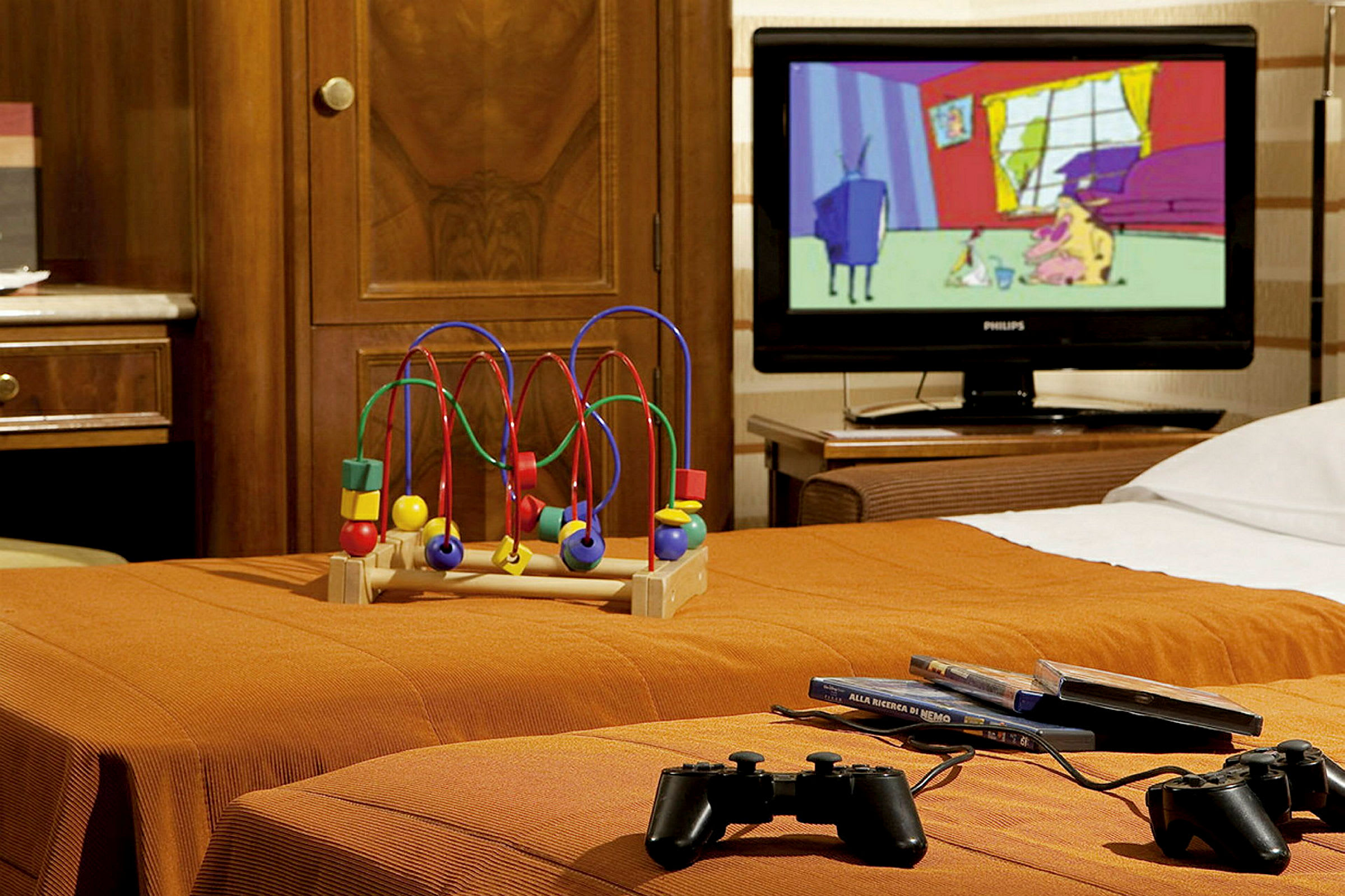 Ett hotellrum med leksak, TV och spelkontroller på en orange säng. (AI-genererad text)