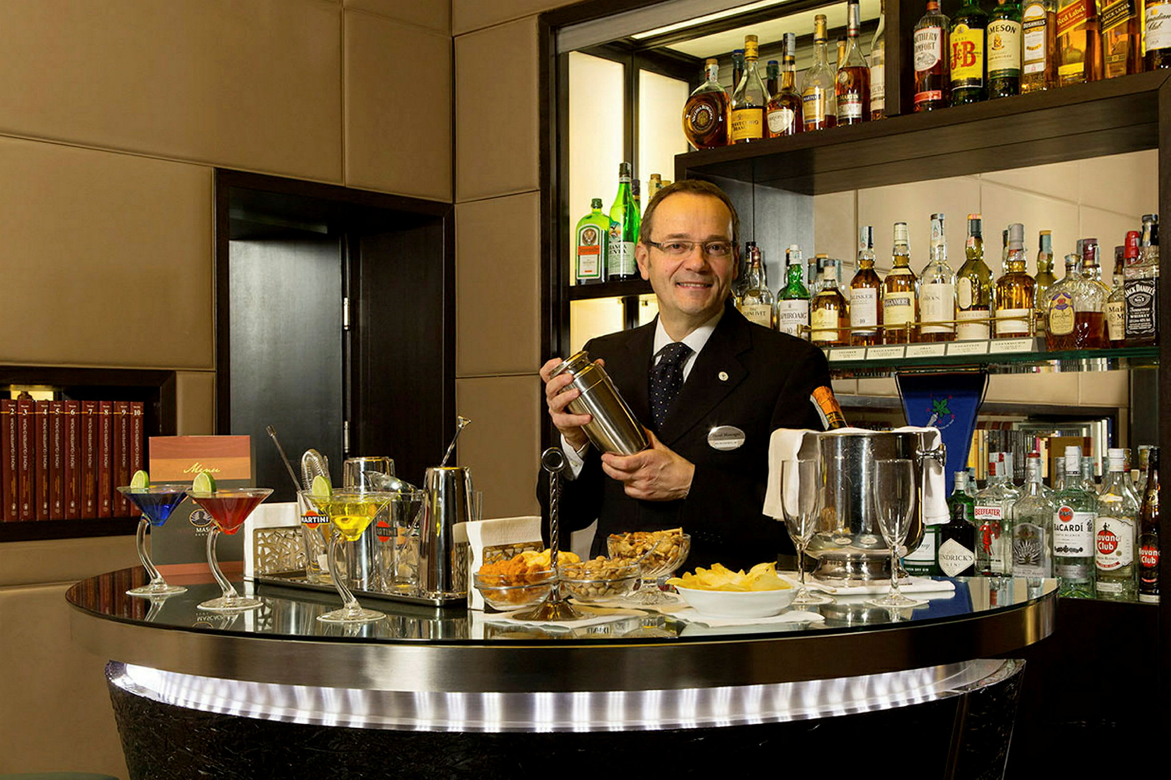 En bartender håller en shaker vid en bardisk fylld med flaskor och cocktails. (AI-genererad text)