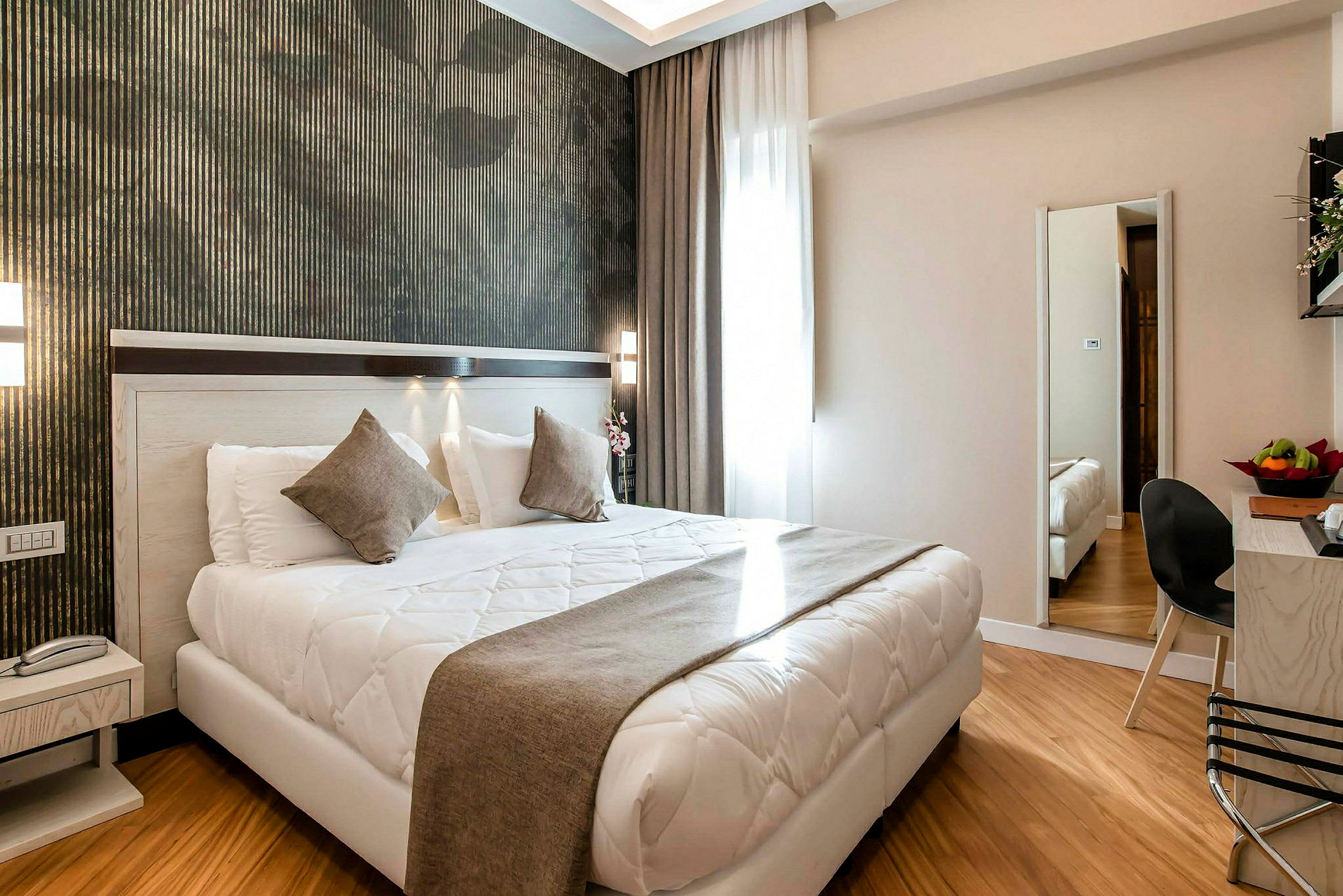 Modernt inrett hotellrum med dubbelsäng, sängbord, spegel och sittområde. (AI-genererad text)