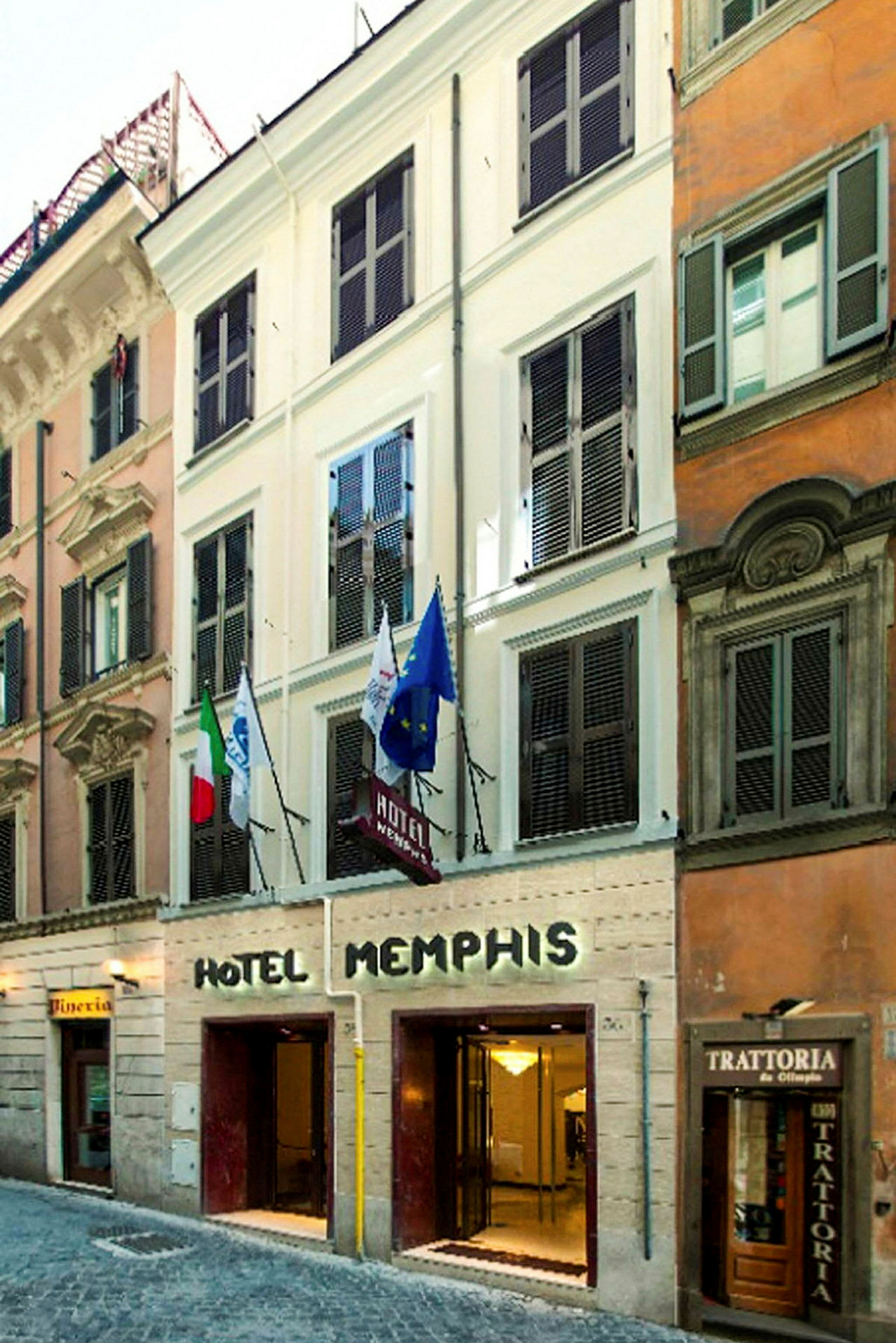 Fasaden av Hotel Memphis med entré på gatuplan och flaggor synliga ovanför. (AI-genererad text)