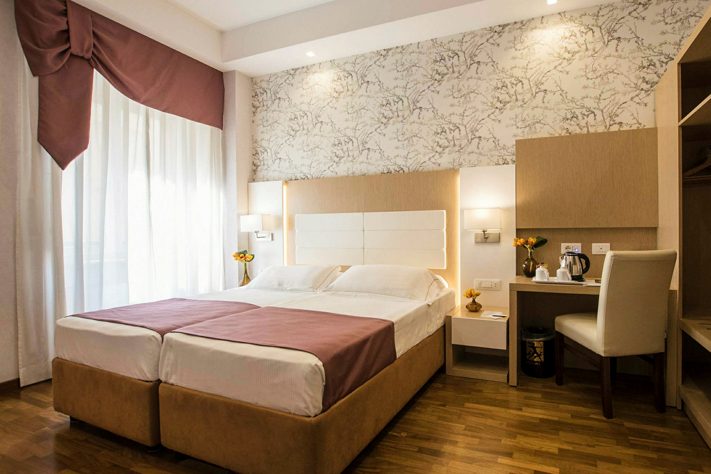 Ett hotellrum med en dubbelsäng, skrivbord och stol, samt dekorativa detaljer. (AI-genererad text)