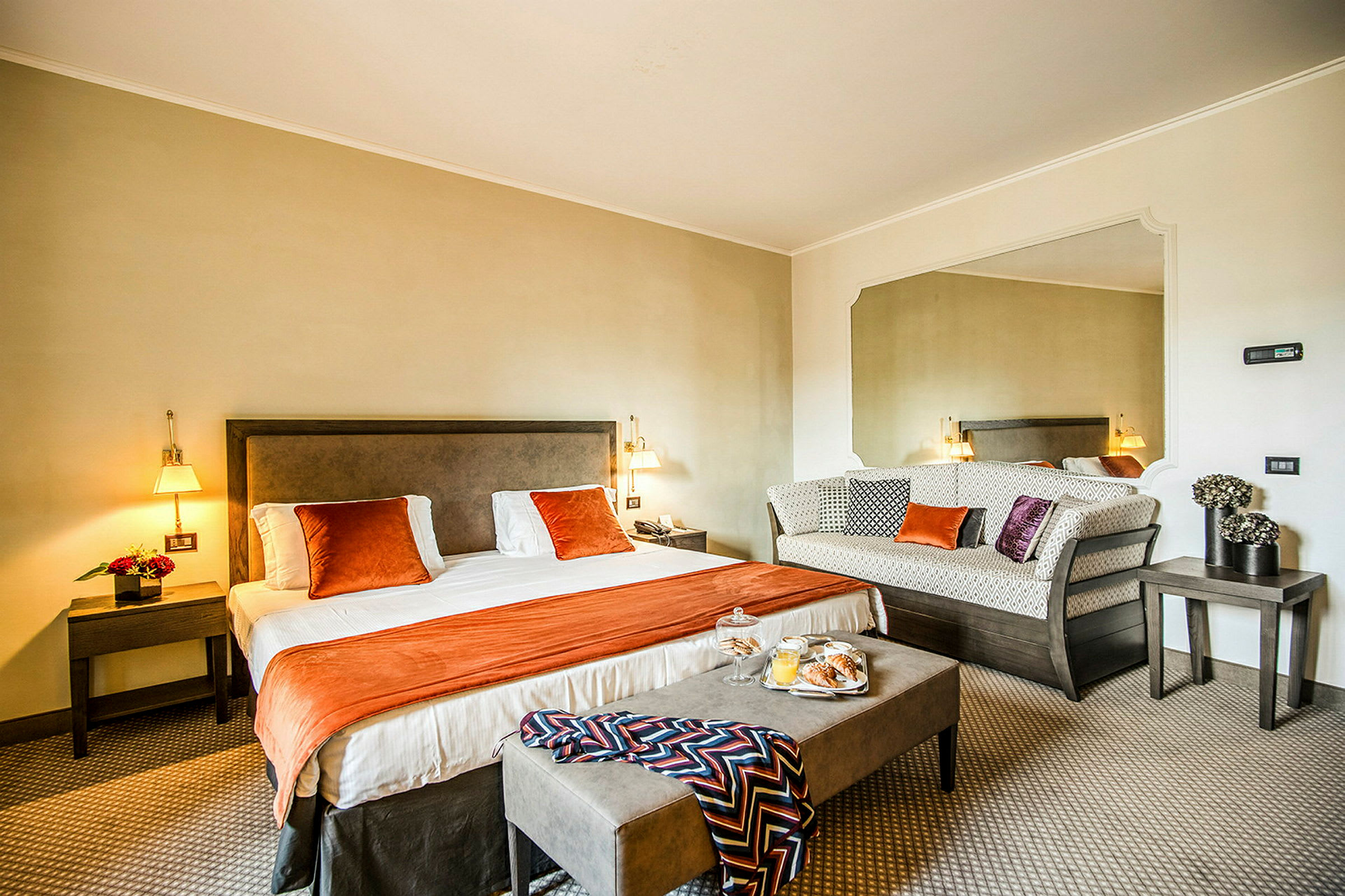 Ett hotellrum med en dubbelsäng, en sittgrupp och en spegel på väggen. (AI-genererad text)