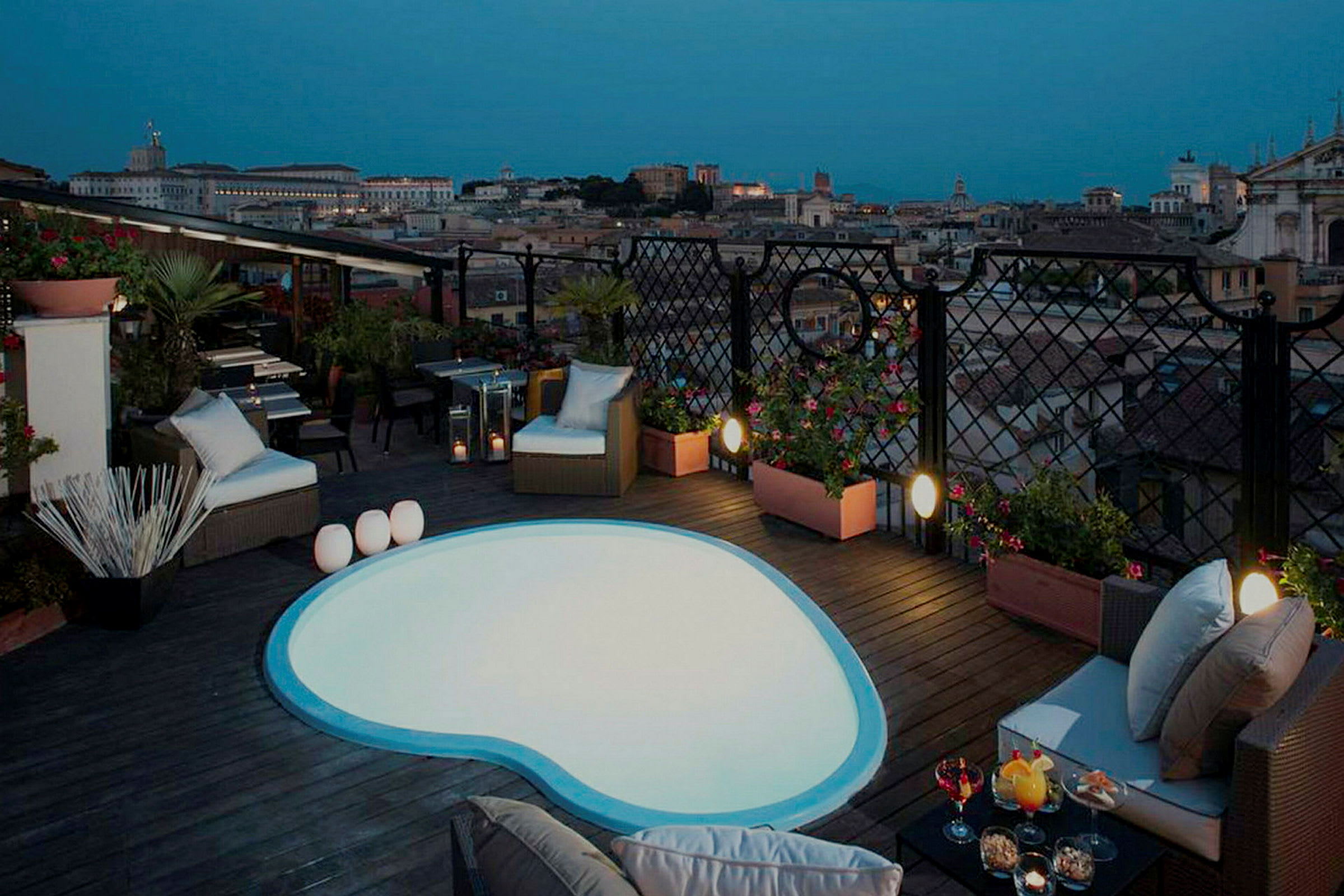 Bild på en takterrass med liten pool och sittmöbler, samt utsikt över en stad i skymning. (AI-genererad text)
