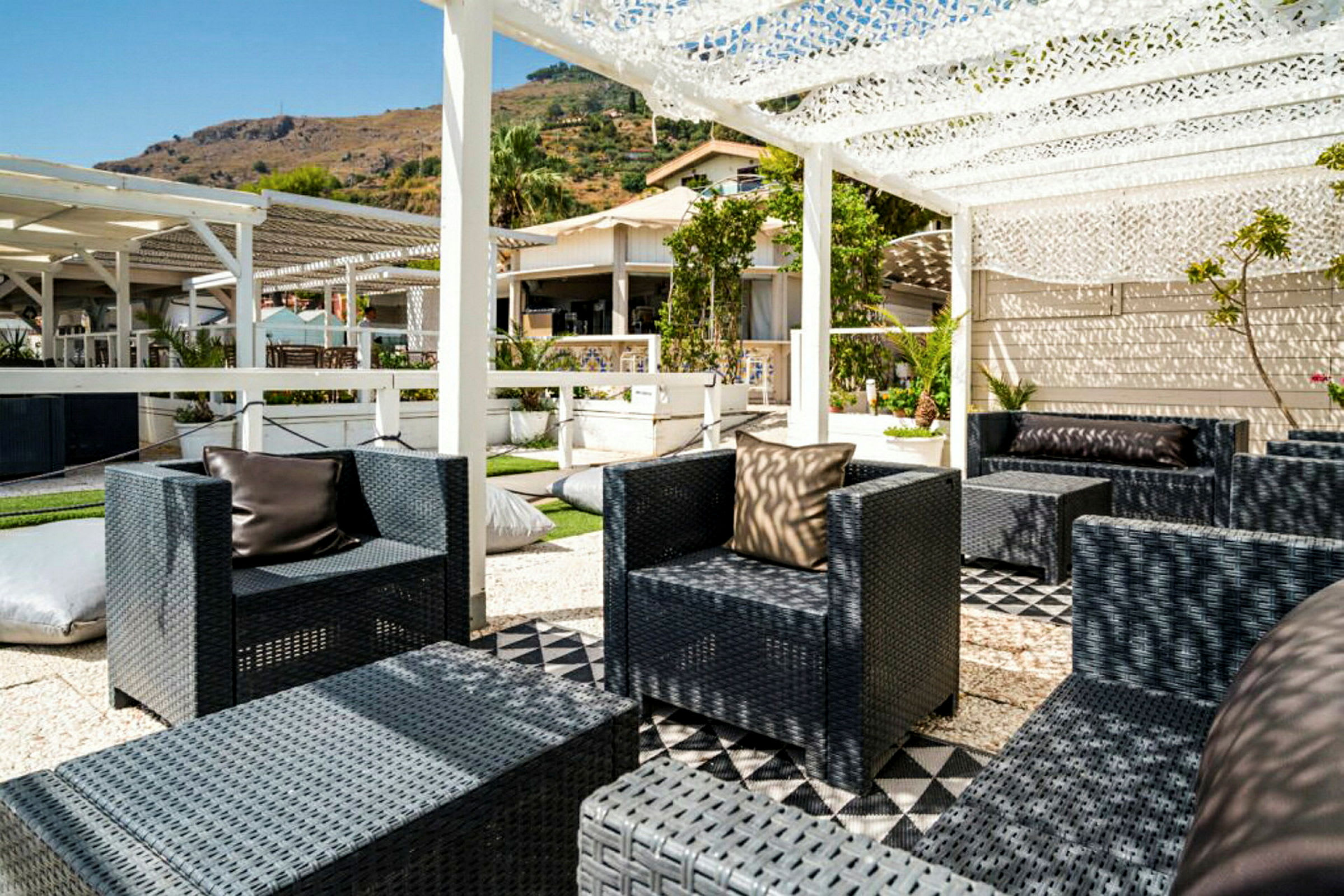 En utomhuslounge med flätade stolar och bord under en pergola. (AI-genererad text)