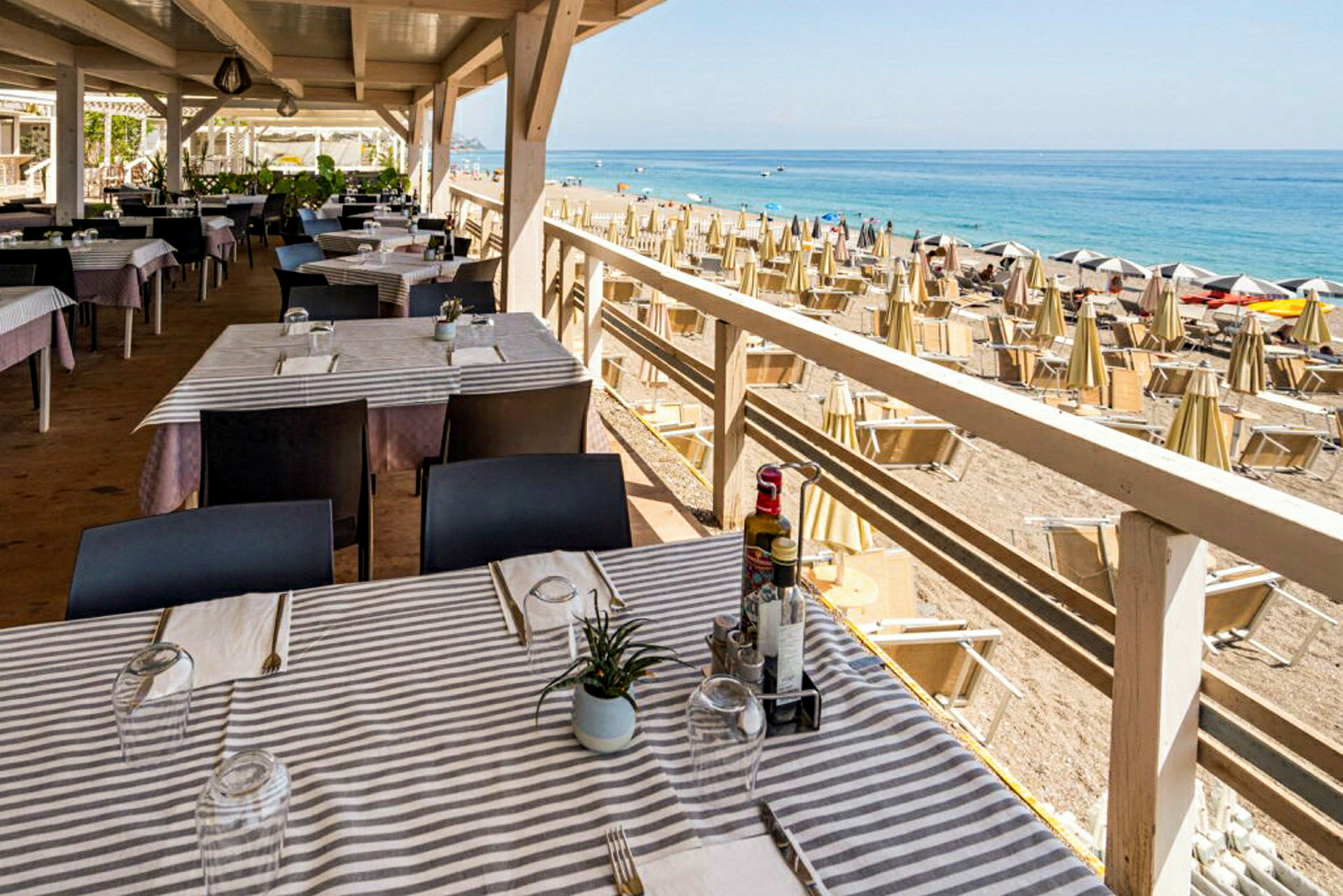En restaurang med dukade bord nära en strand med parasoller och solstolar. (AI-genererad text)