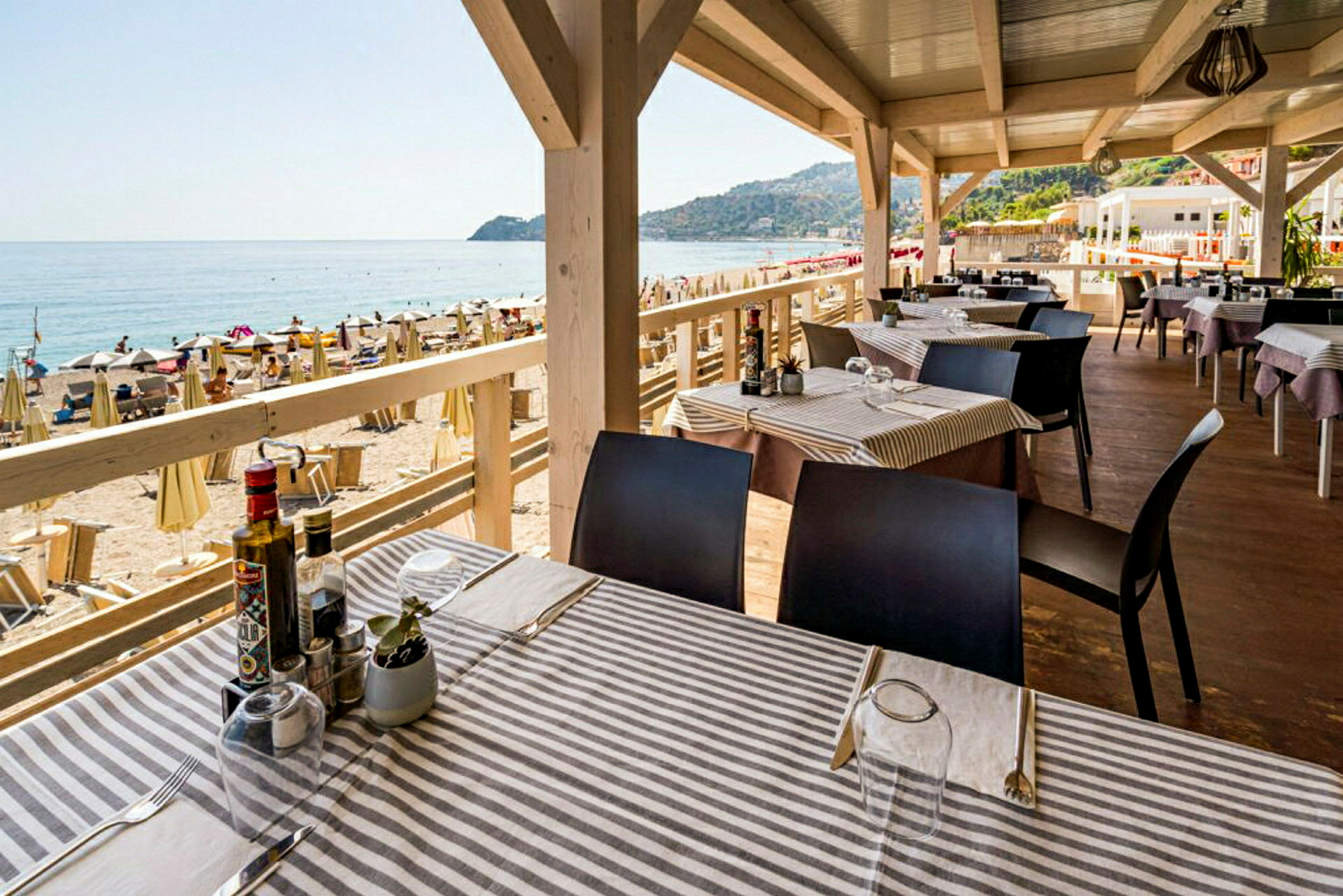 En strandrestaurang med utsikt över havet och stranden, med dukade bord och solstolar i bakgrunden. (AI-genererad text)