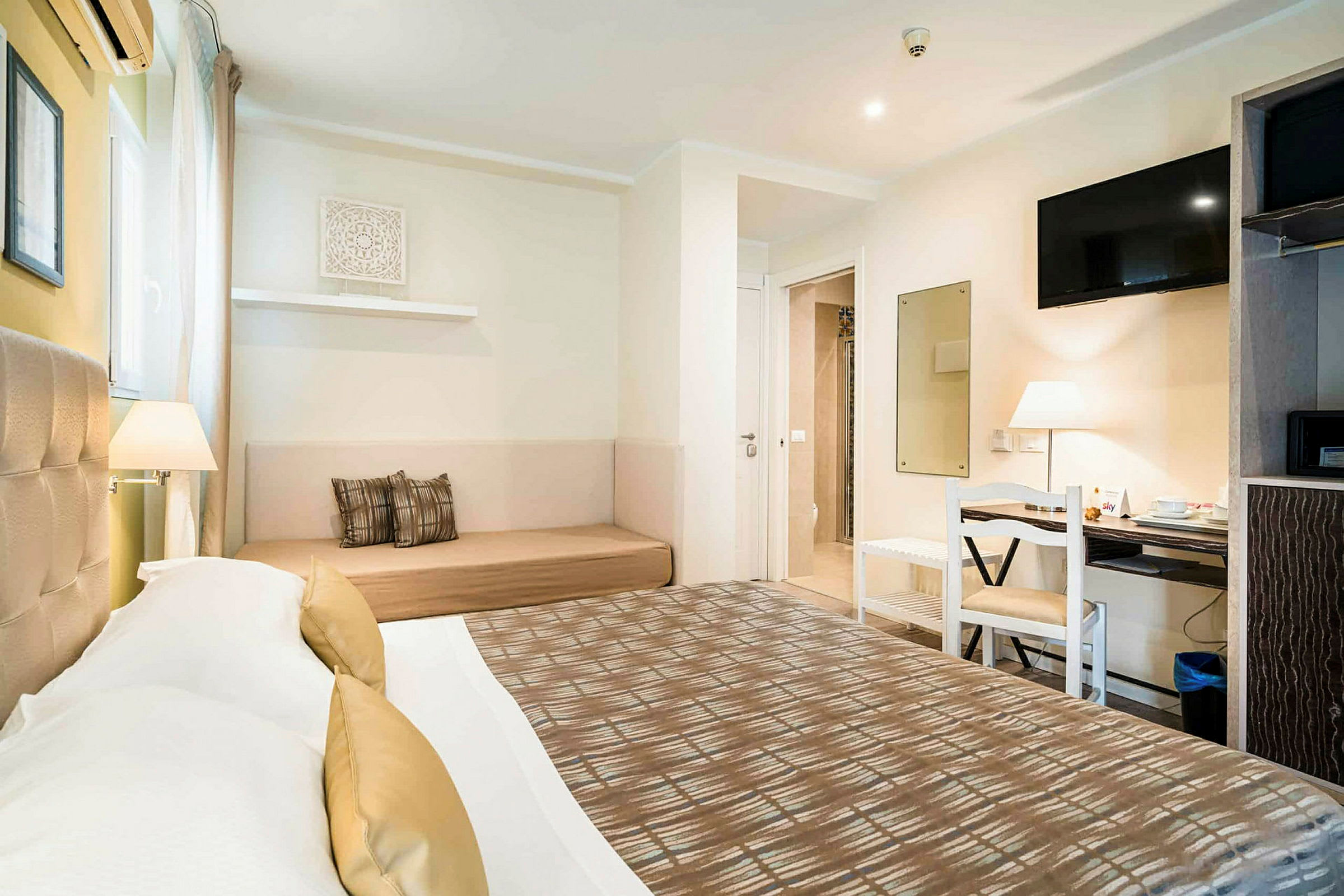 Ett hotellrum med en dubbelsäng, en soffa, ett skrivbord med stol och en väggmonterad TV. (AI-genererad text)