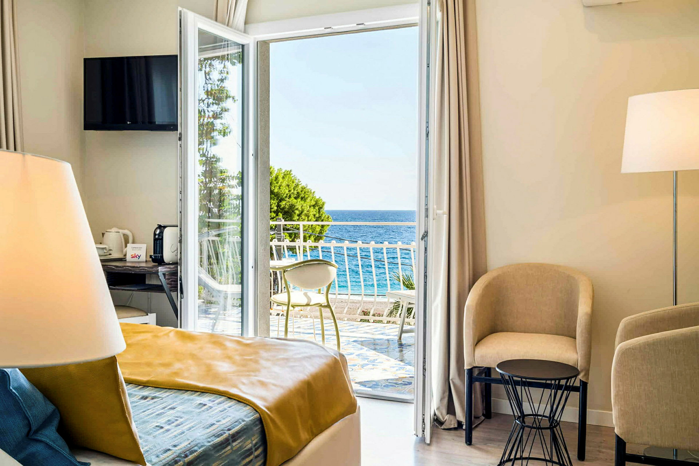 Ett ljust hotellrum med utsikt mot havet genom en öppen balkongdörr. (AI-genererad text)