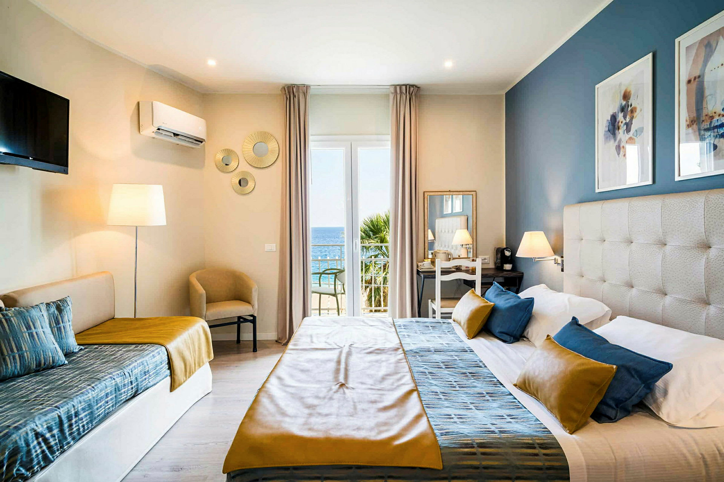 Ett hotellrum med en säng, en soffa, och utsikt mot havet genom en glasdörr. (AI-genererad text)
