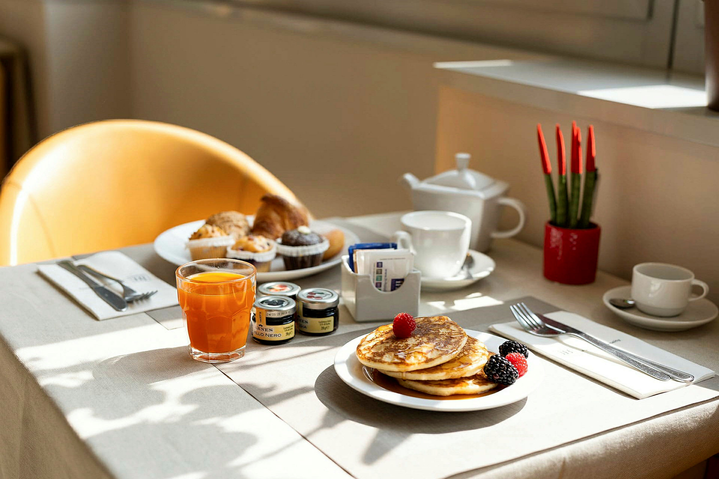 En dukad frukost med pannkakor, frukt, juice och muffins på ett bord. (AI-genererad text)