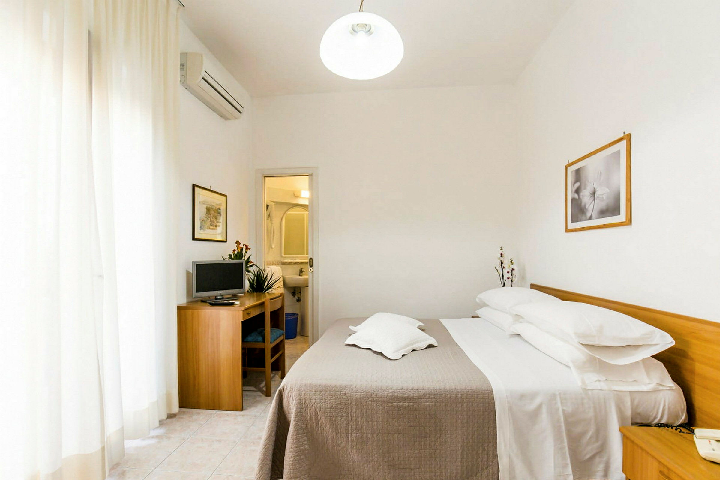 Ett hotellrum med en dubbelsäng, ett skrivbord med en TV och en ingång till ett badrum. (AI-genererad text)