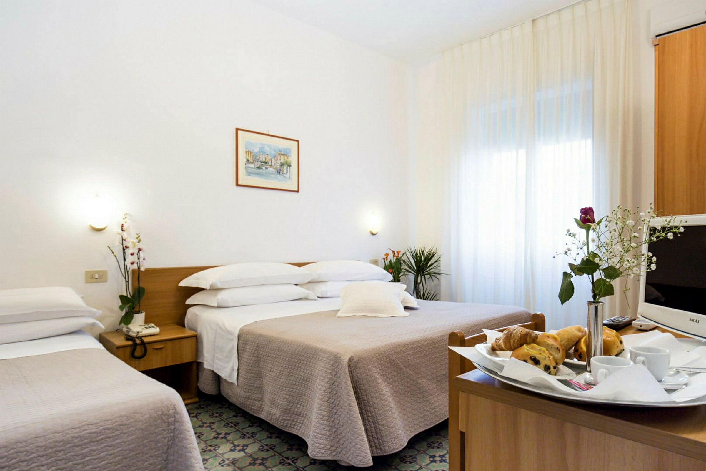Ett hotellrum med en dubbelsäng, en enkelsäng och ett bord med frukost och en vas med blommor. (AI-genererad text)