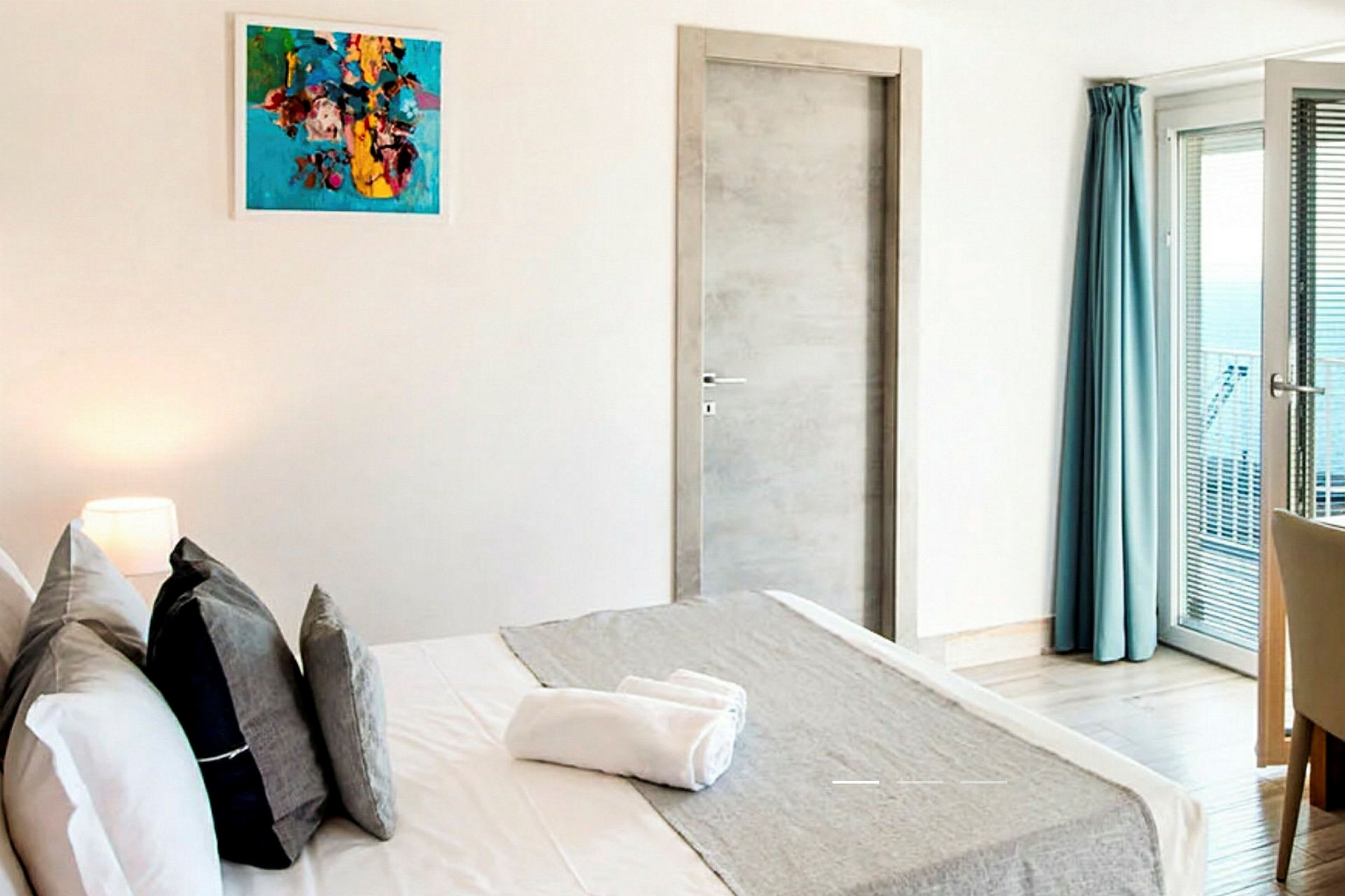 Modernt hotellrum med en dubbelsäng, konst på väggen, garderob och ett fönster med blå gardiner. (AI-genererad text)