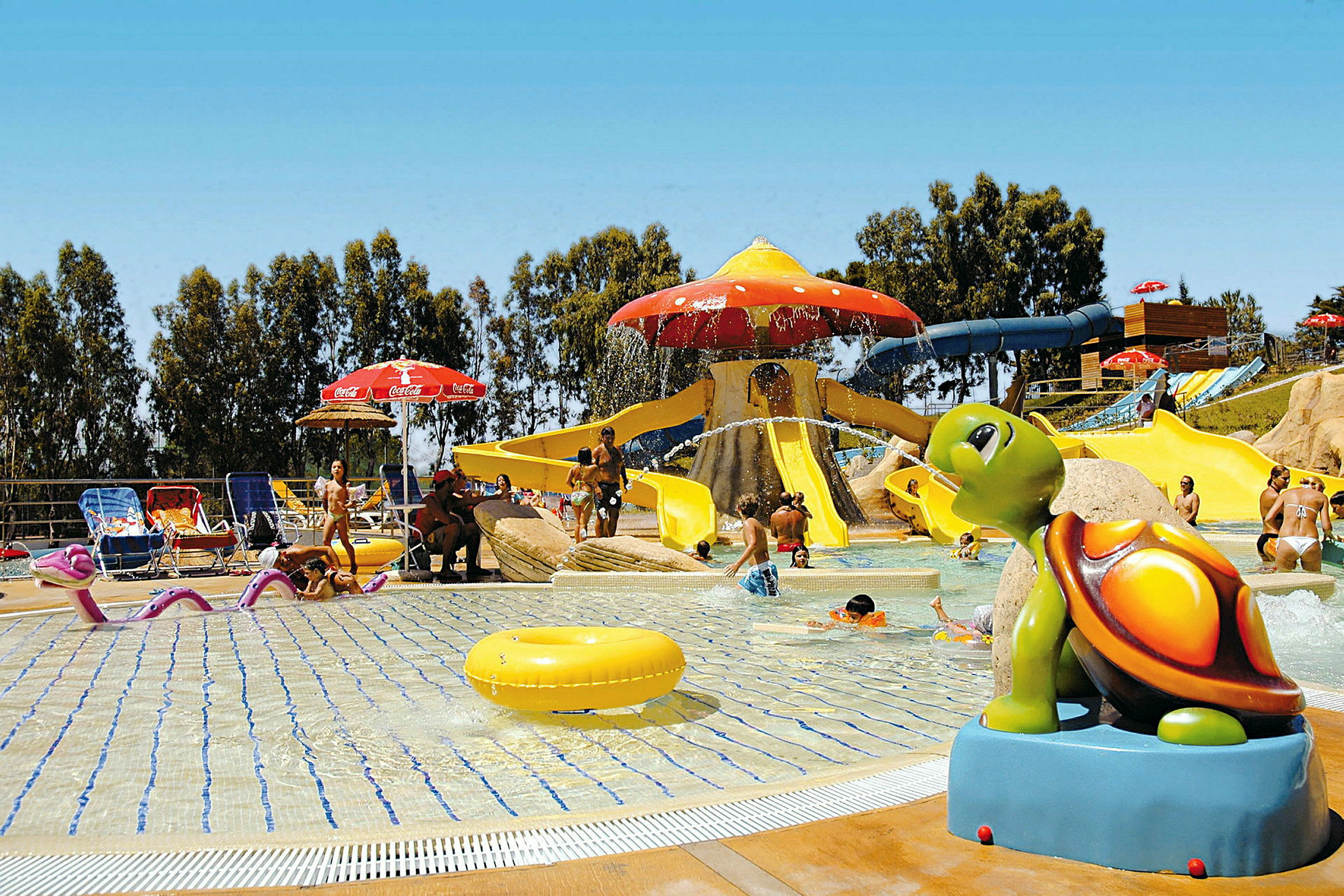 Bilden visar en vattenpark med en grund pool och flera vattenrutschbanor, samt en skulptur av en färgglad sköldpadda. (AI-genererad text)
