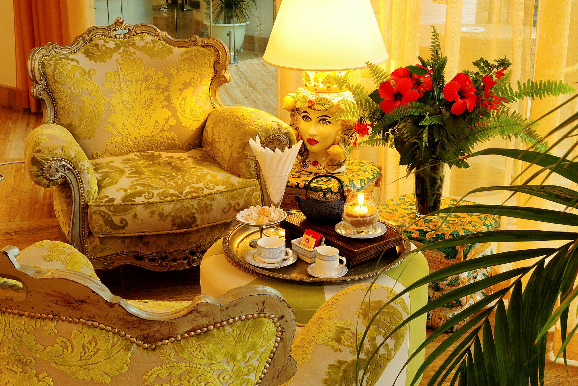 Ett klassiskt möblerat rum med guldfärgade fåtöljer. På bordet finns en bricka med tekoppar, teapot och ljus, samt en vas med röda blommor. (AI-genererad text)