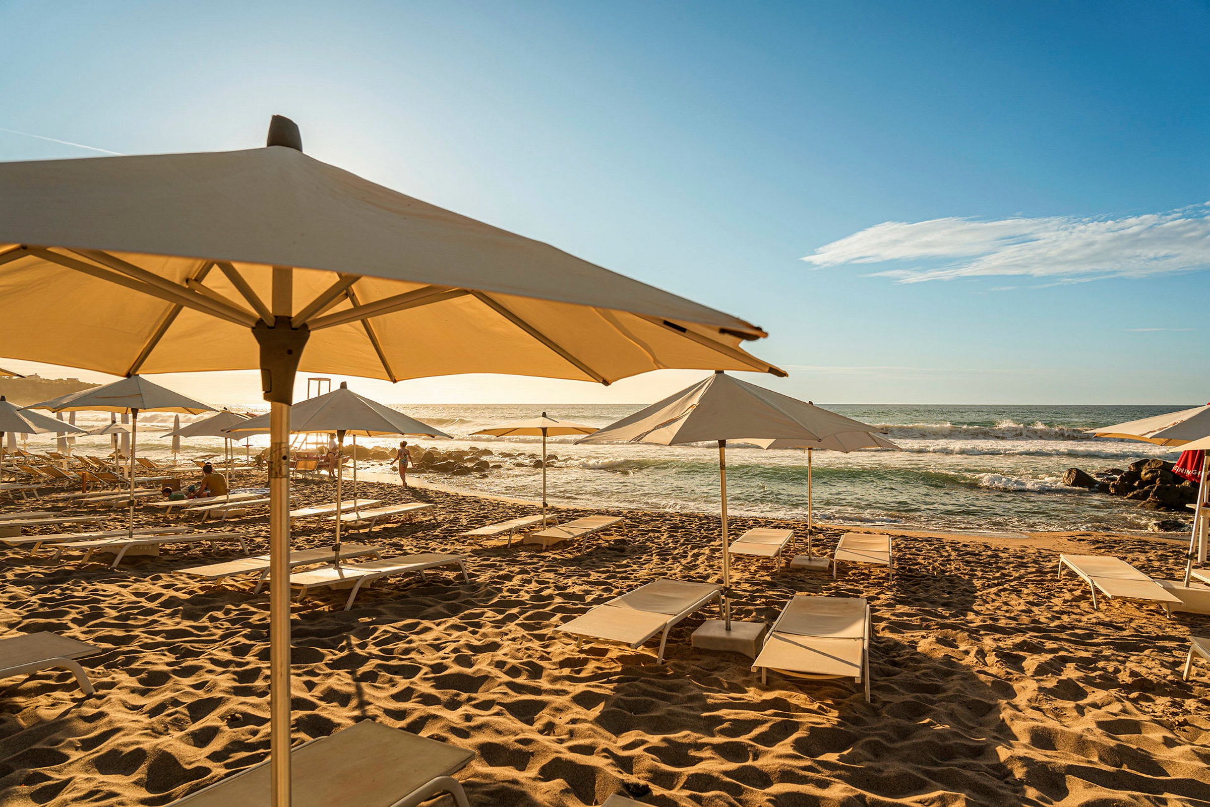 Solstolar med parasoller står uppställda på en sandstrand vid havet. (AI-genererad text)