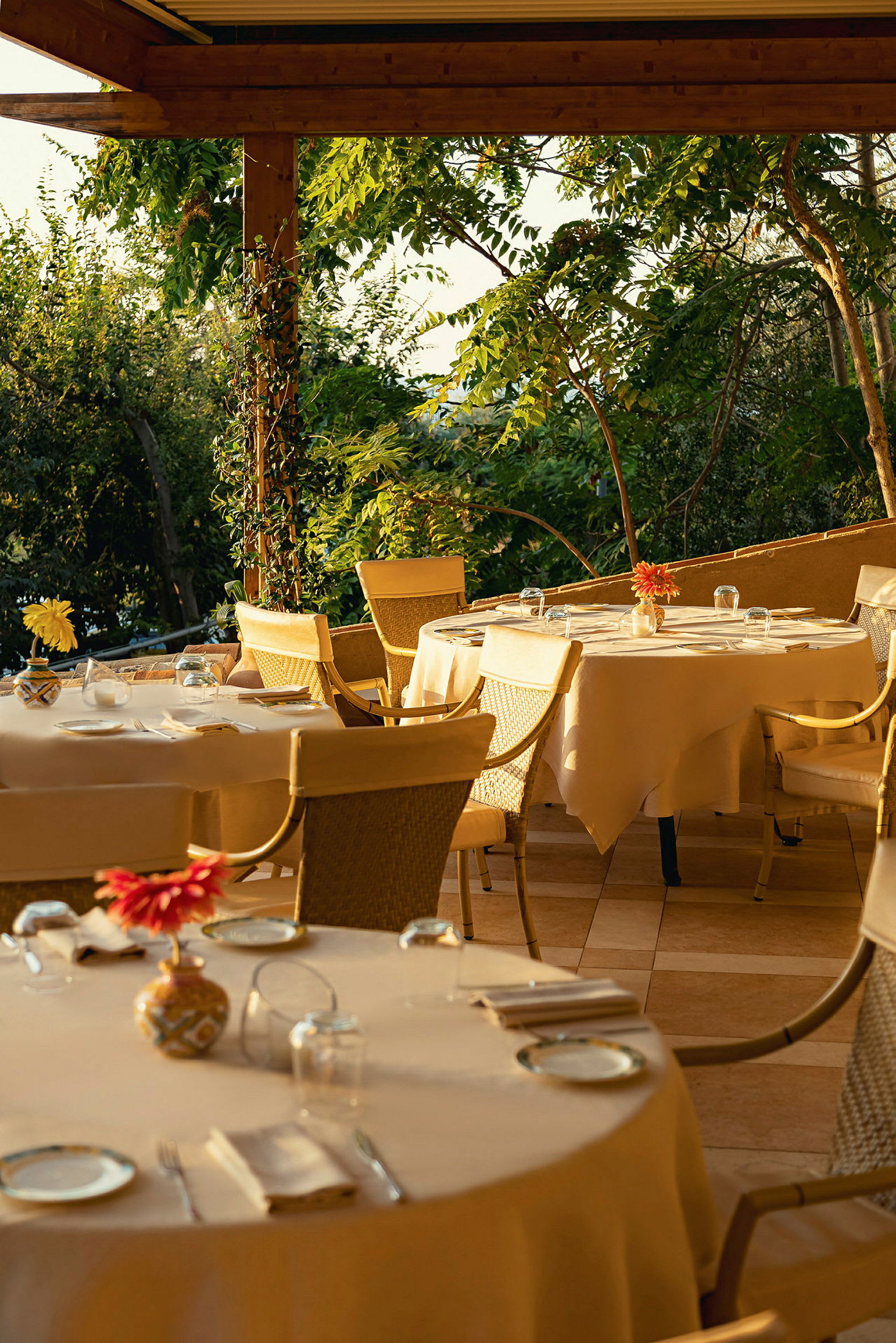 Uteservering med dukade bord och stolar under en träpergola, med utsikt över grönska. (AI-genererad text)
