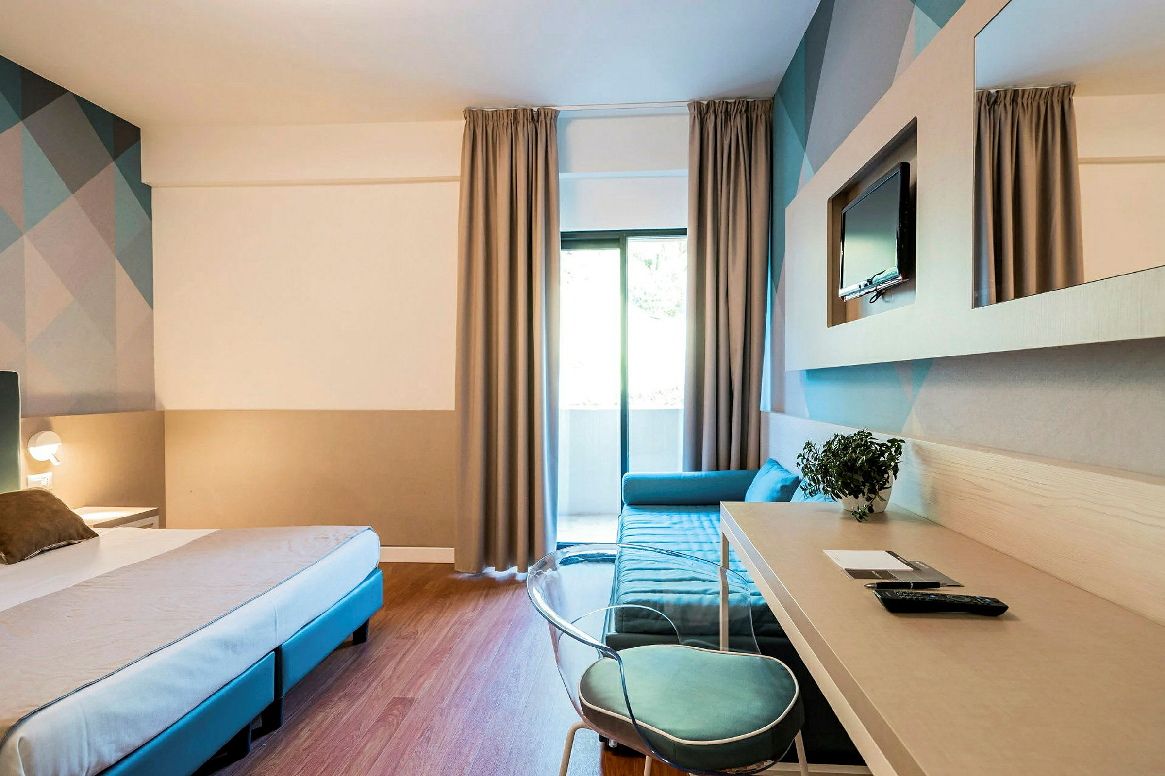 Hotellrum med säng, skrivbord och soffa, samt TV på väggen. (AI-genererad text)