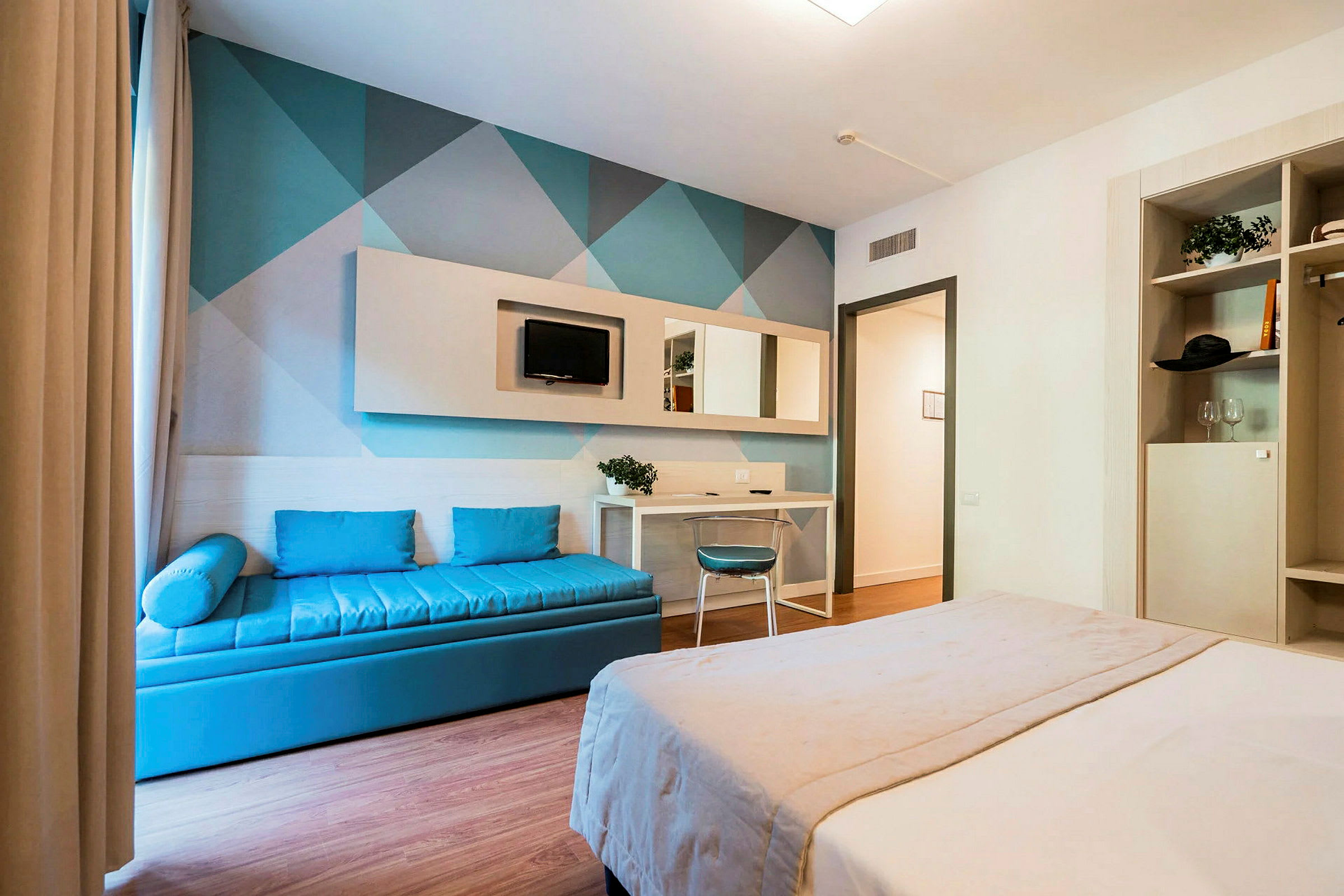 Ett hotellrum med en dubbelsäng, en blå soffa och en skrivbordshörna. (AI-genererad text)
