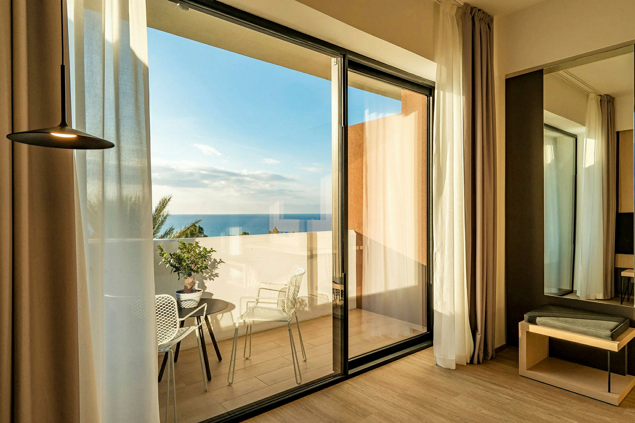 Hotellrum med glasdörrar som leder ut till en terrass med havsutsikt. (AI-genererad text)