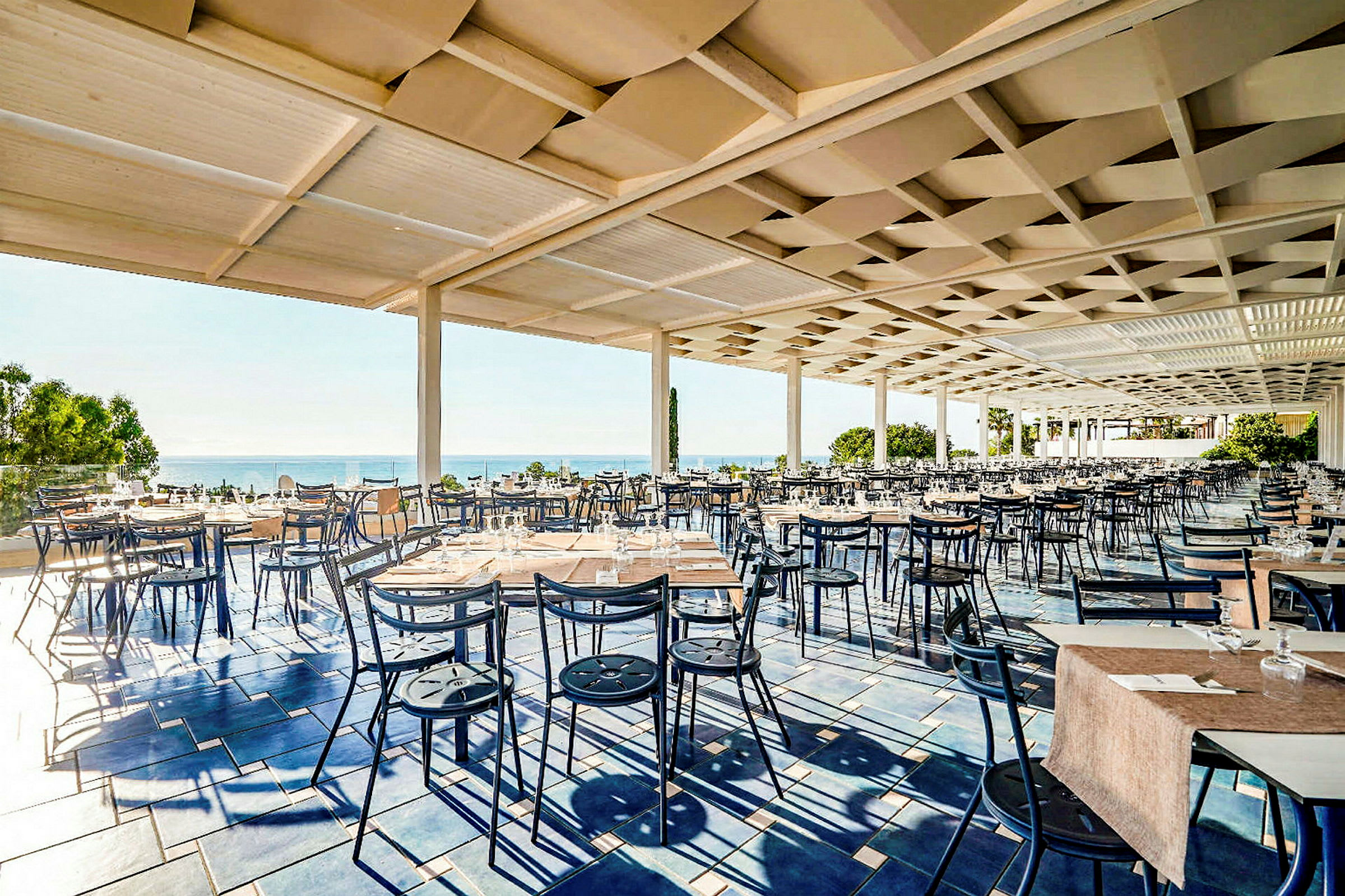 Utomhus restaurang med många bord och stolar, belägen nära havet. (AI-genererad text)