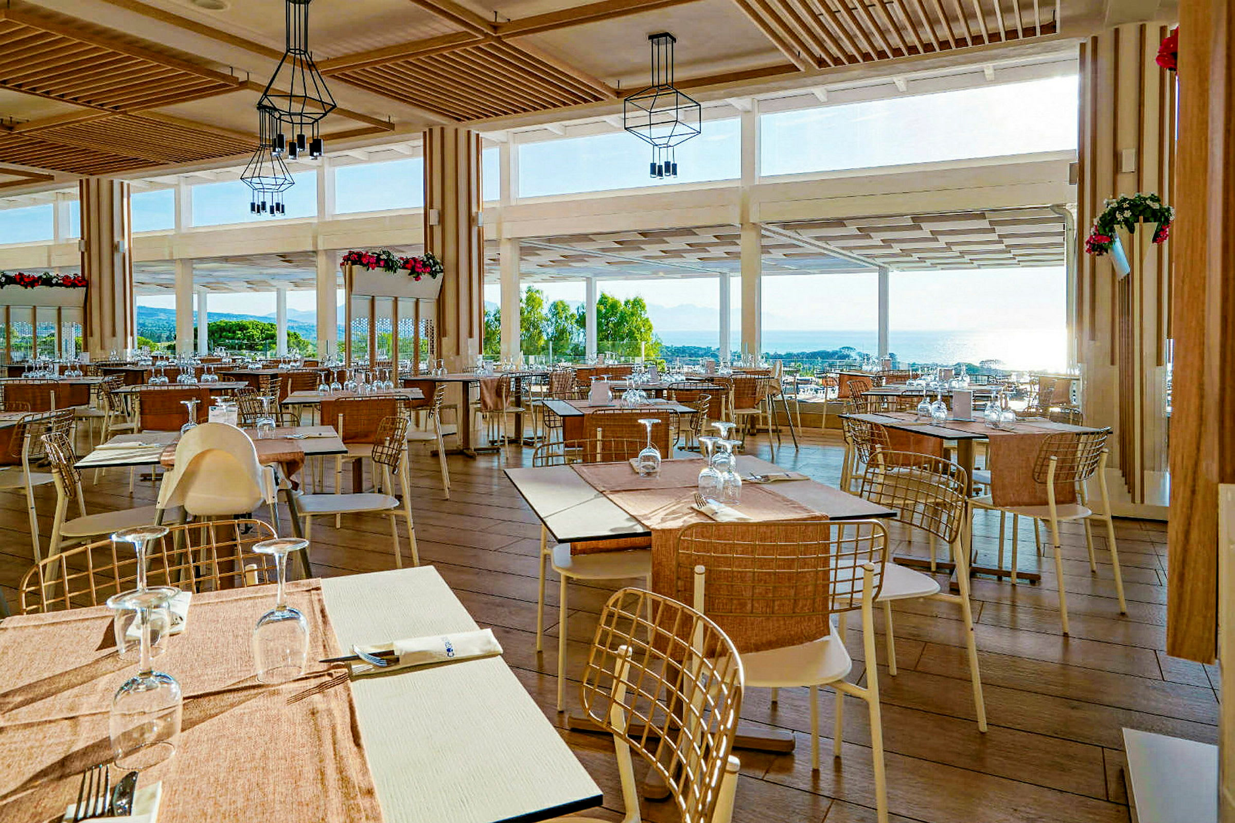 En restaurang med bord och stolar, stora fönster med utsikt över landskapet och havet. (AI-genererad text)