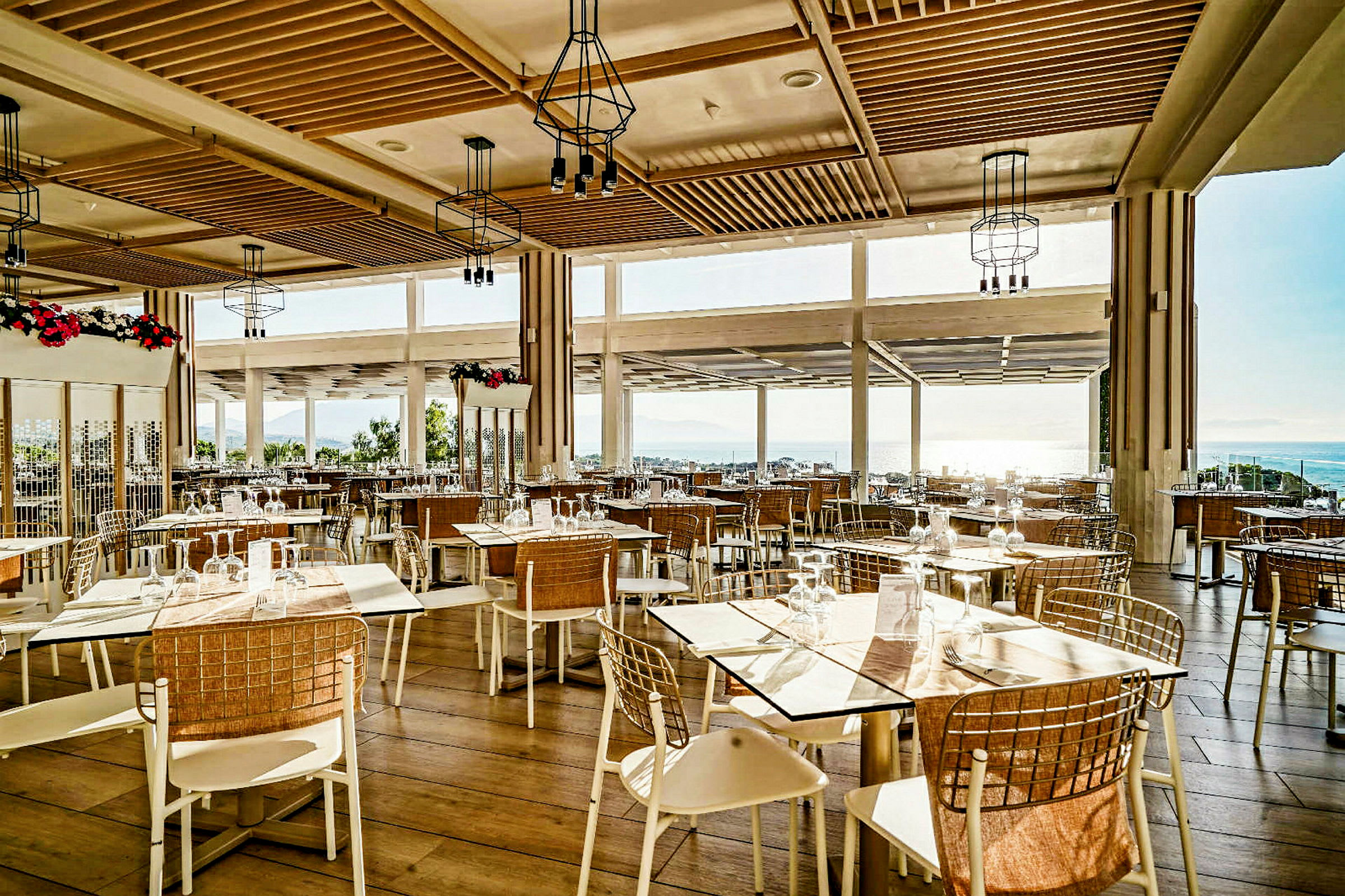 Restaurang med stora fönster och trädetaljer, uppställda bord och stolar. (AI-genererad text)