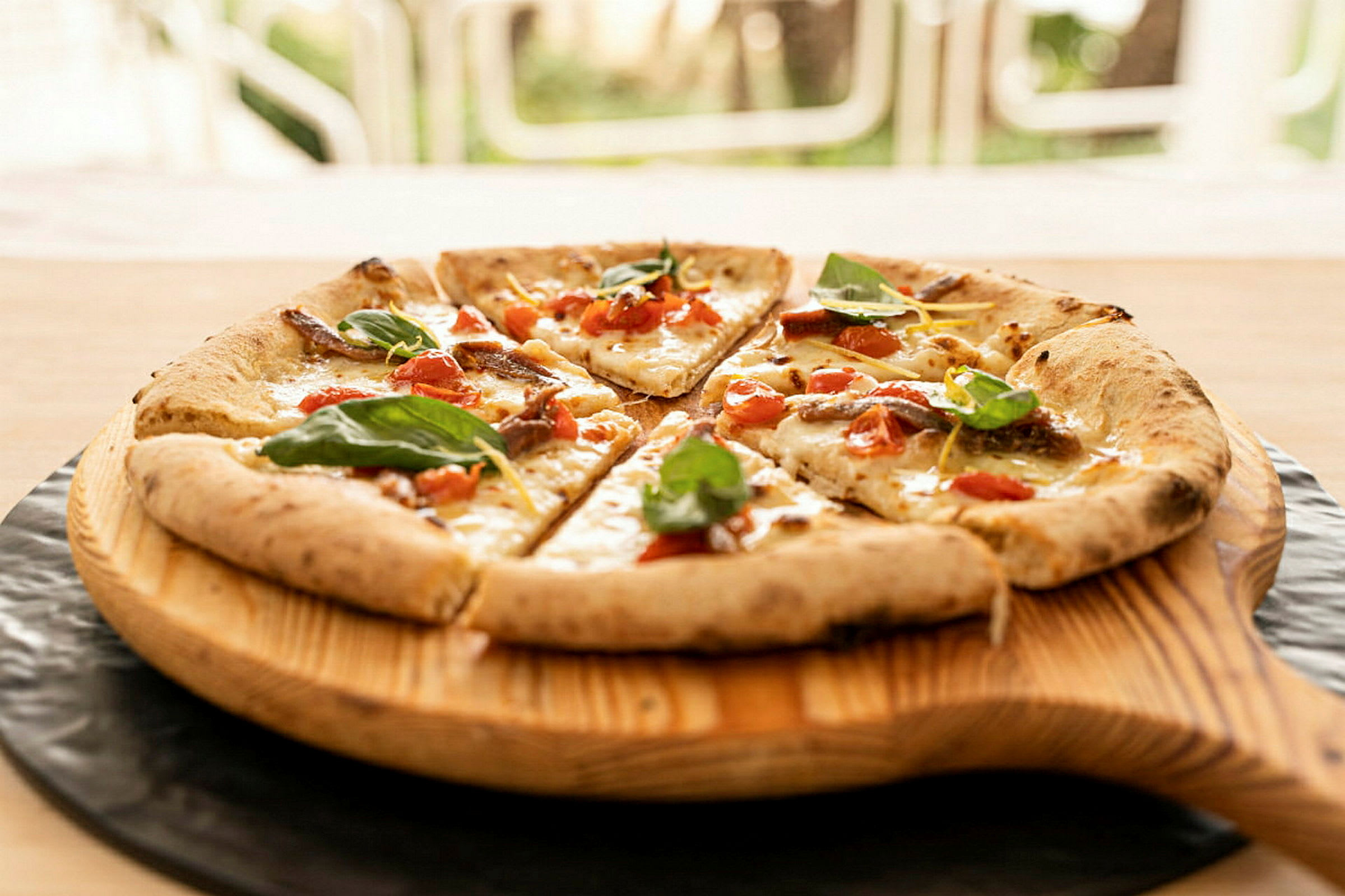 En pizza med tomat, ost och bladkryddor serverad på en träbricka. (AI-genererad text)