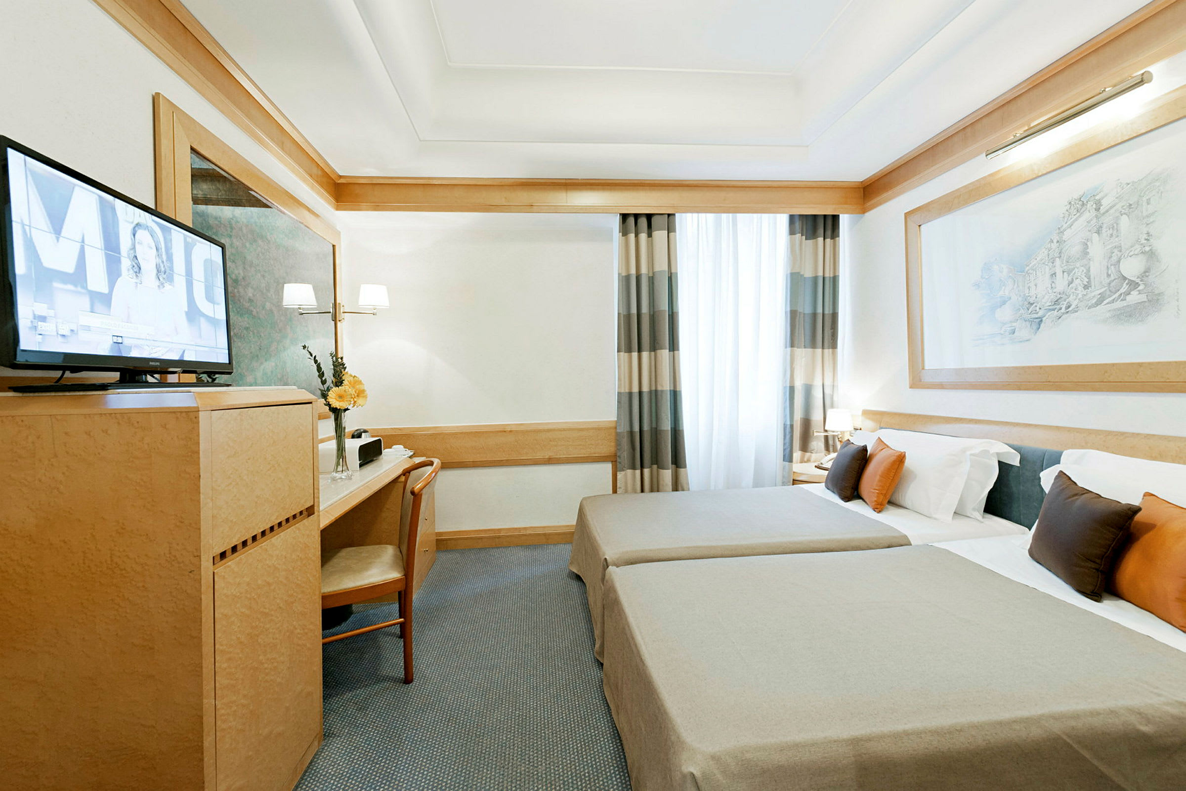 Ett hotellrum med två enkelsängar, en skrivbordshörna, en väggmonterad TV och en stor fönsterdraperi. (AI-genererad text)