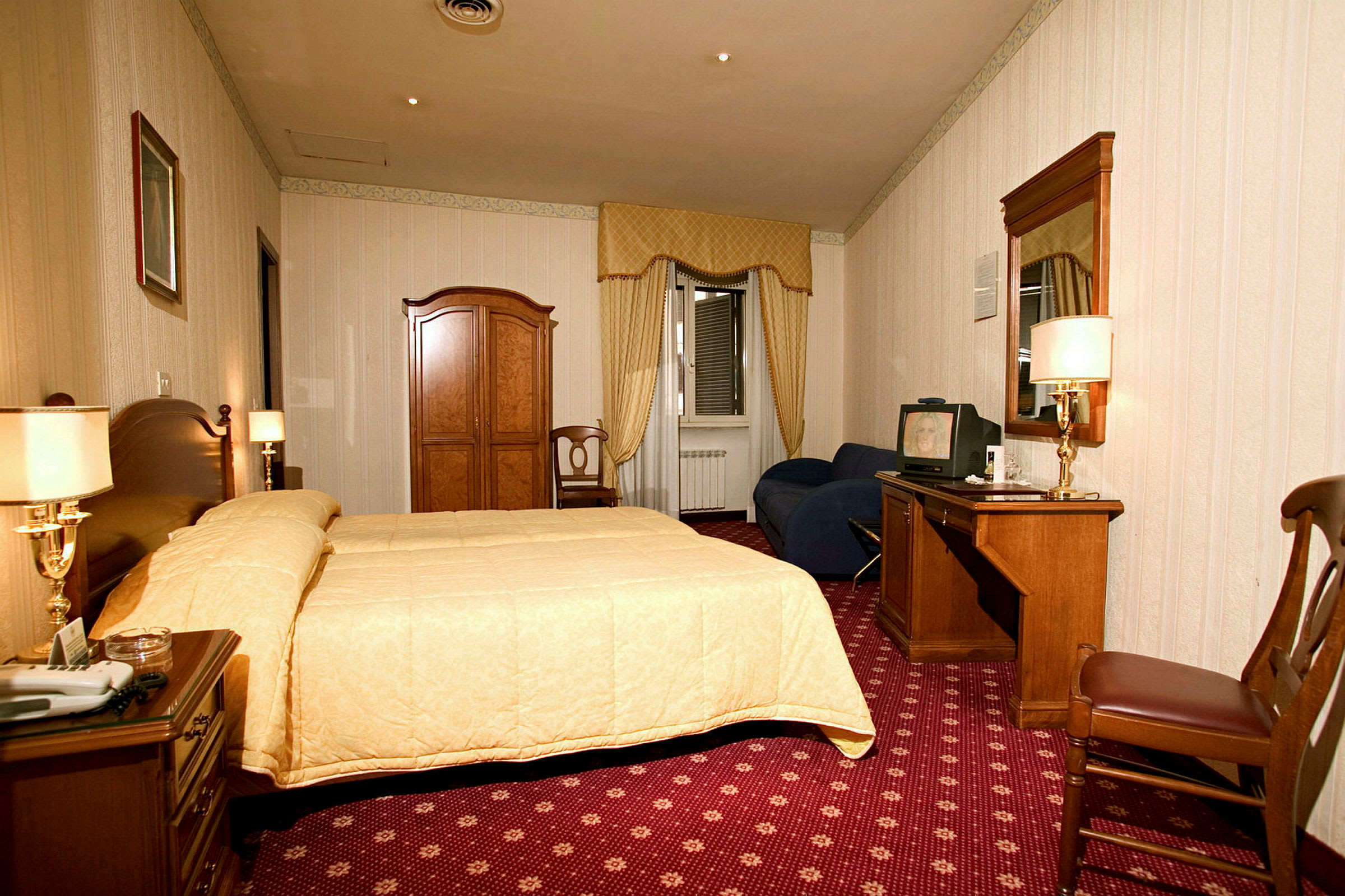 Ett hotellrum med en säng, ett skrivbord, en garderob och ett fönster med draperier. (AI-genererad text)