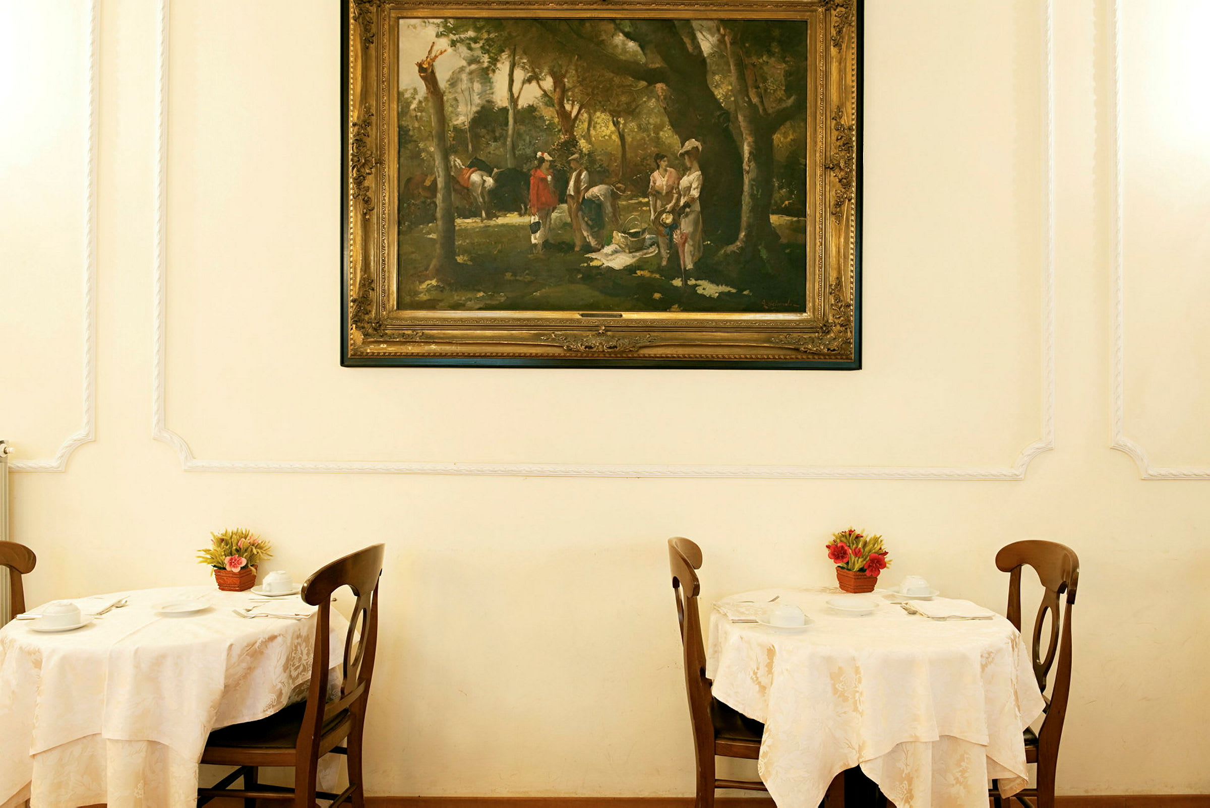 Ett rum med två dukade bord med stolar, dekorerade med blomkrukor och ett stort inramat konstverk på väggen. (AI-genererad text)