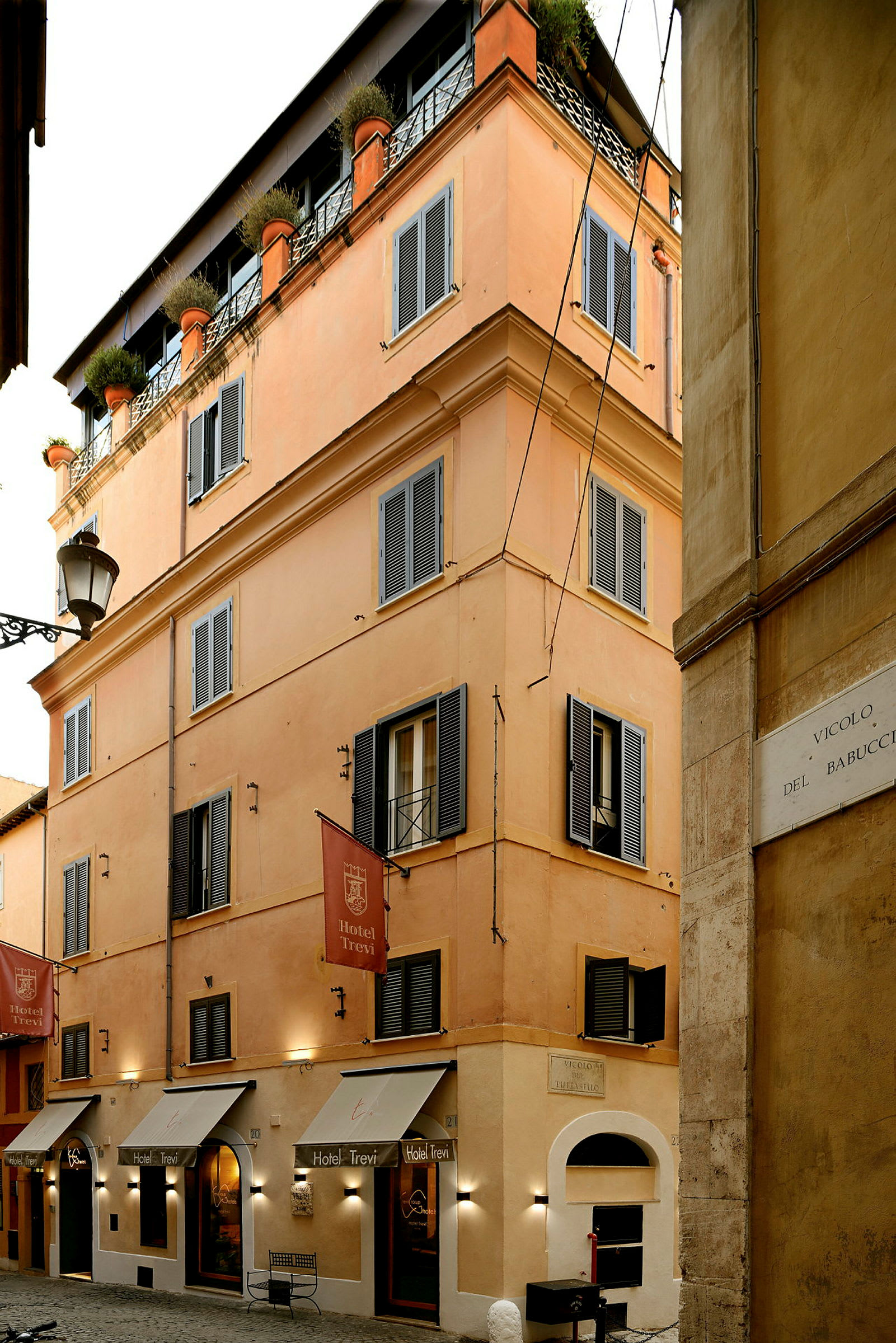 En byggnad med orange fasad, mörka fönsterluckor och skyltar med texten 'Hotel Trevi'. (AI-genererad text)