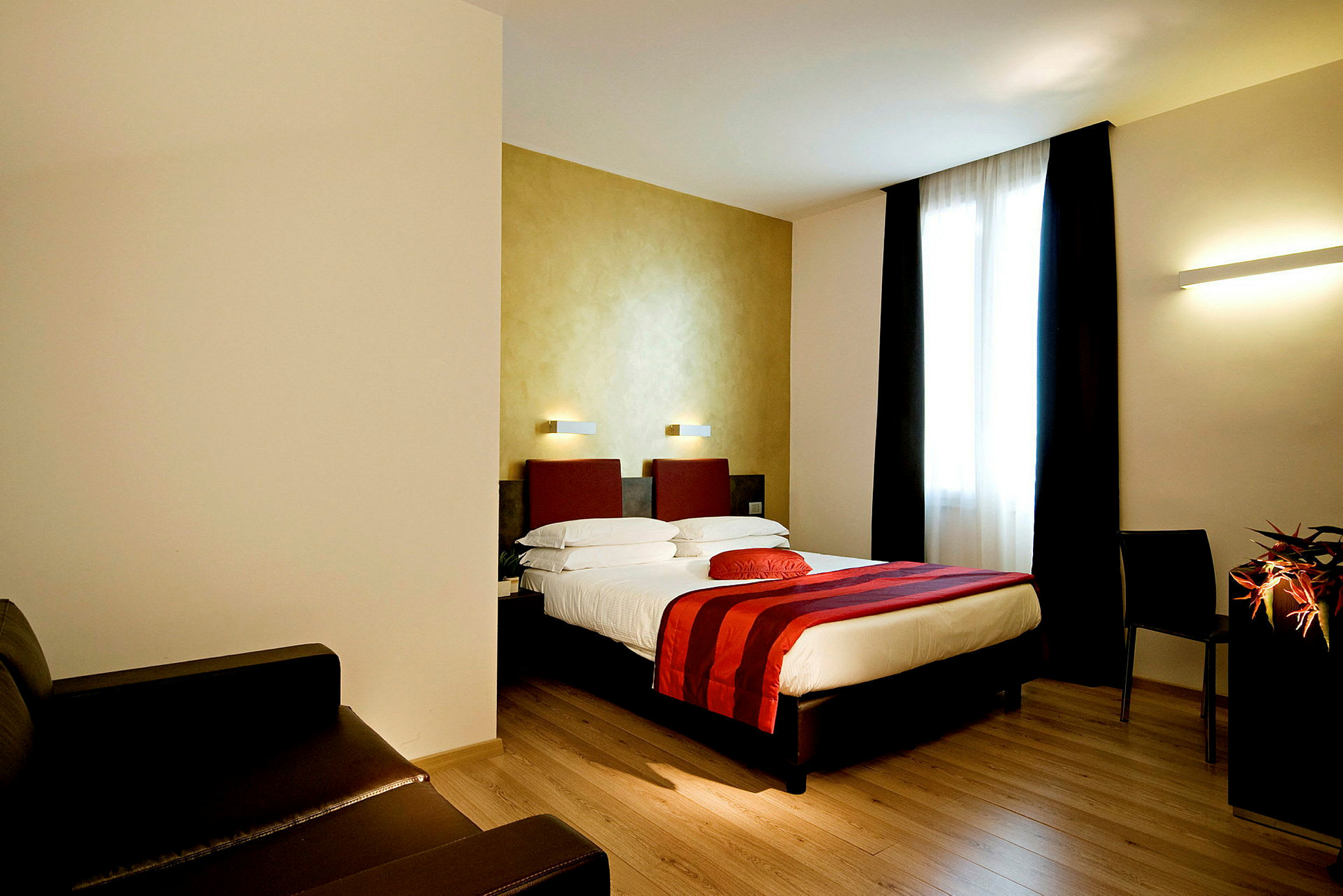 Ett hotellrum med en dubbelsäng, röda detaljer och stort fönster. (AI-genererad text)