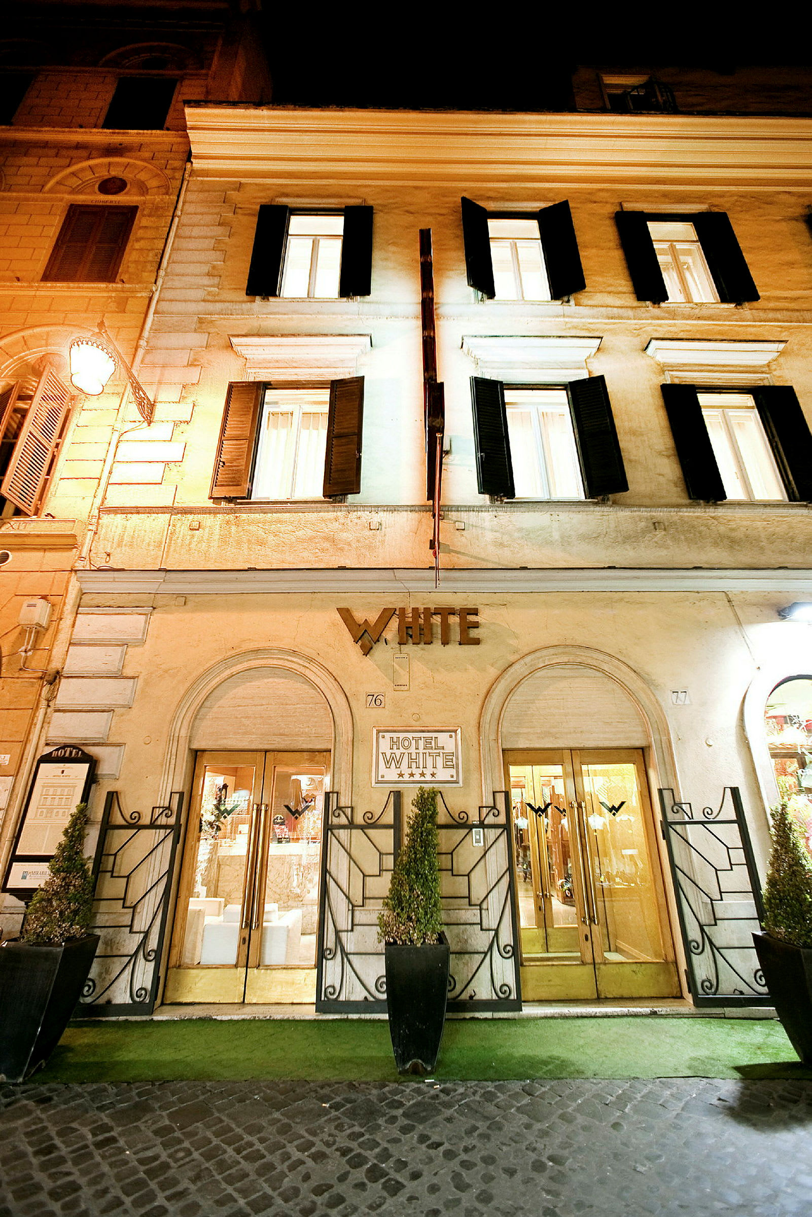 Hotellets fasad med namnet 'White' över ingången, markerade dörröppningar och dekorerande växter. (AI-genererad text)