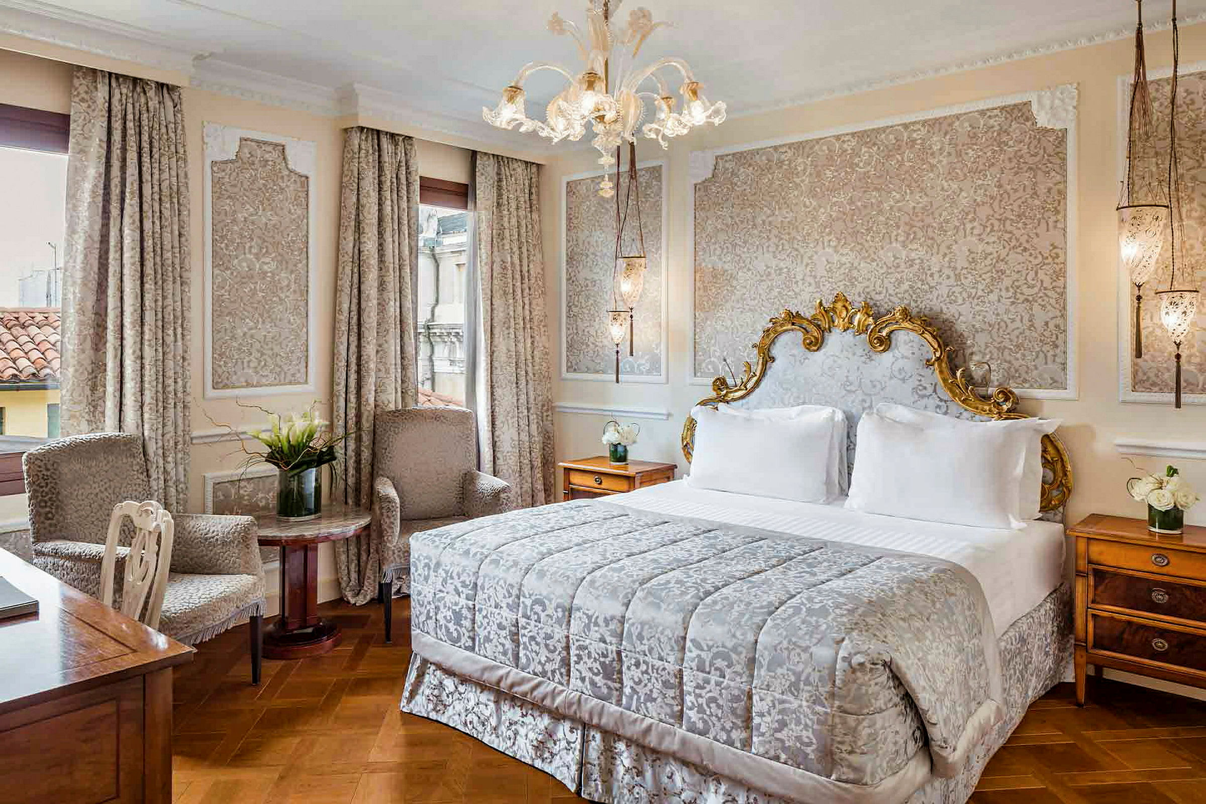 Ett elegant sovrum med en stor säng med dekorerad sänggavel, två fåtöljer, och ett bord med en vas med blommor. (AI-genererad text)