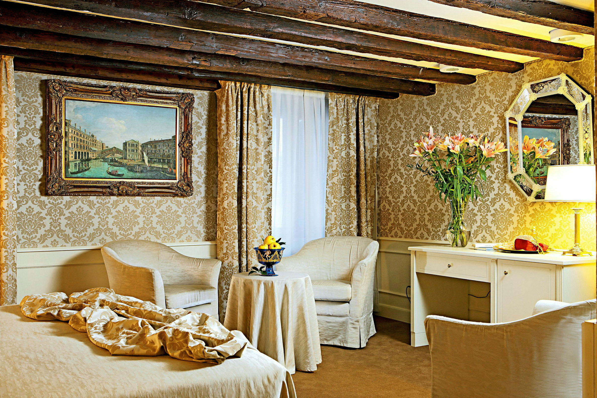 Ett elegant hotellrum med klassisk inredning inklusive två fåtöljer, bord, skrivbord och väggdekorationer. (AI-genererad text)