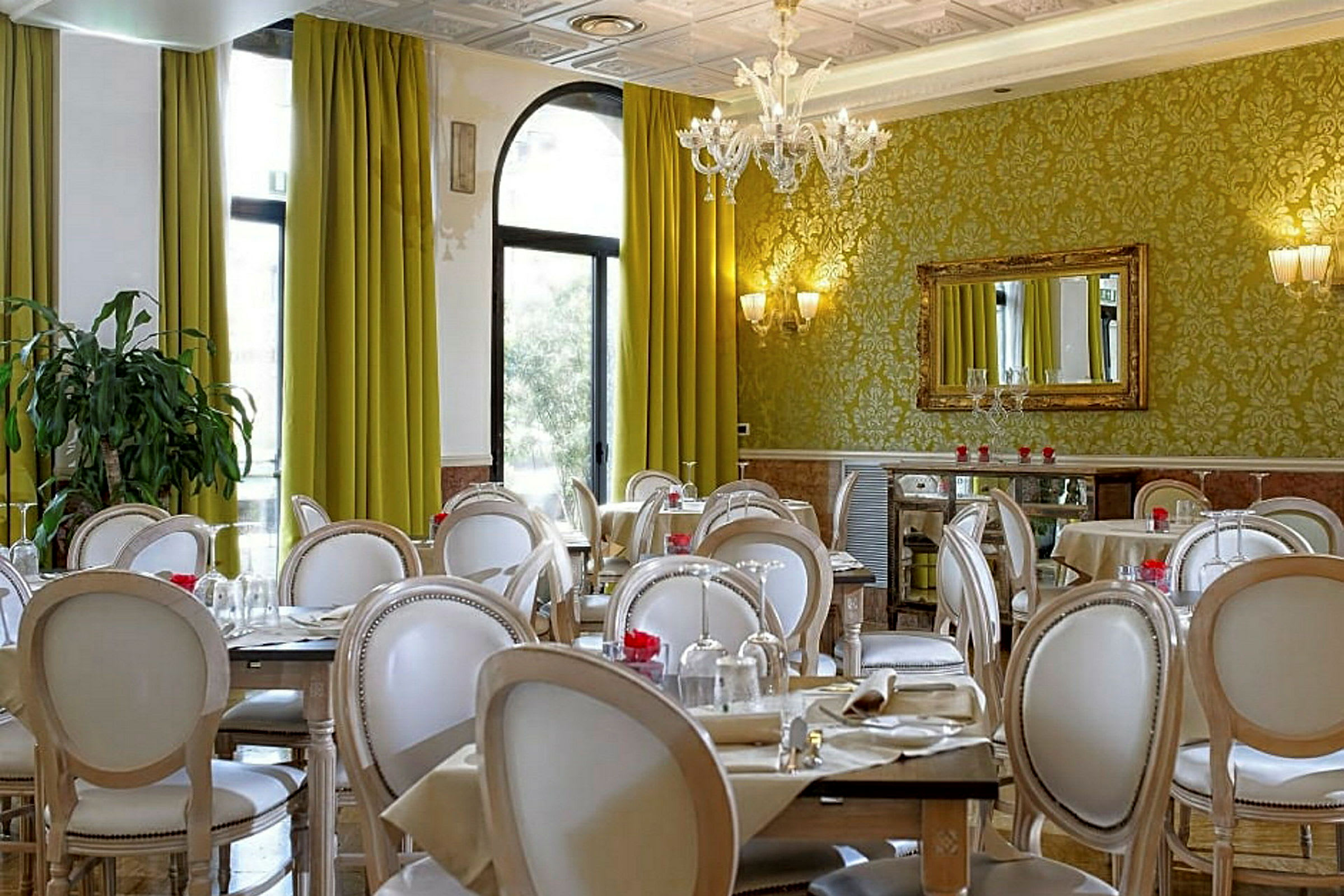 Ett elegant inrett restaurangområde med gröna gardiner, dekorerade väggar och vita stolar runt dukade bord. (AI-genererad text)