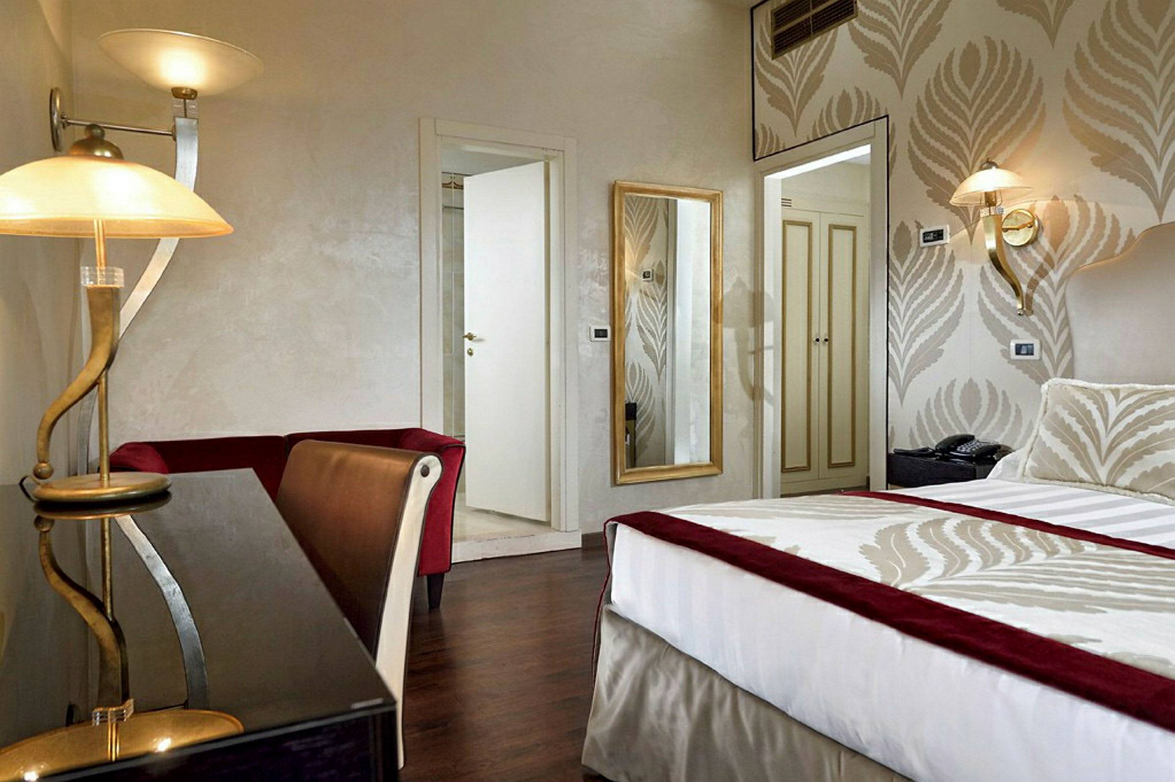 Ett hotellrum med en säng, bord, spegel och en öppen dörr. (AI-genererad text)