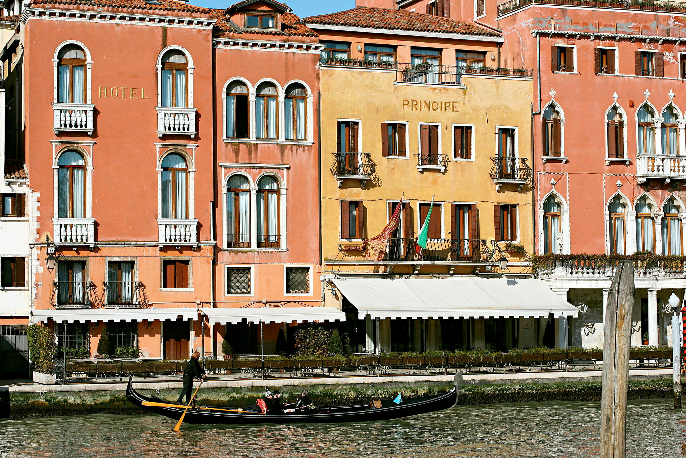 Bild av fasaderna på färgglada byggnader vid en kanal i Venedig med en gondol i vattnet. (AI-genererad text)