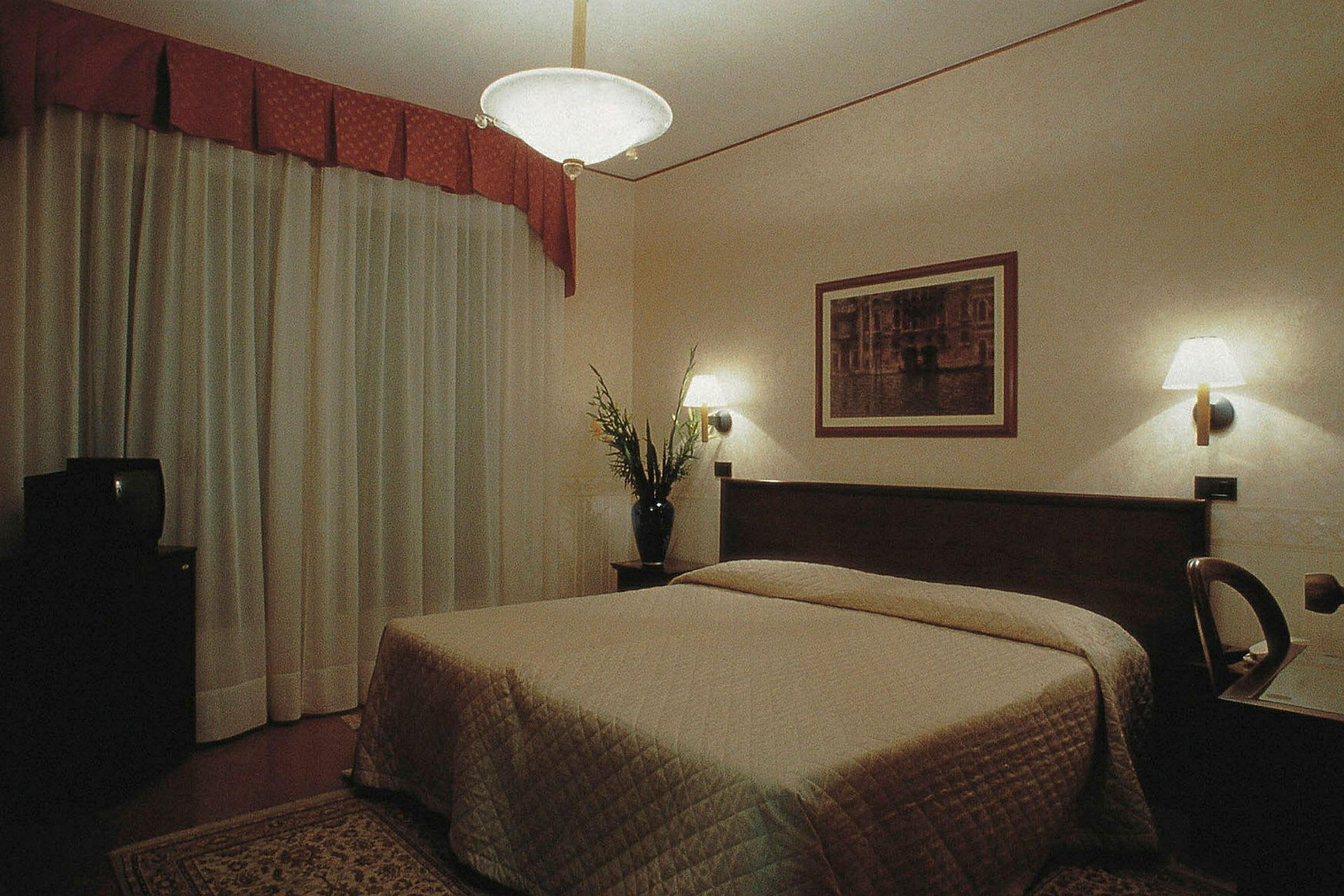 Ett hotellrum med en dubbelsäng, vägglampor och en tavla ovanför sängen. (AI-genererad text)