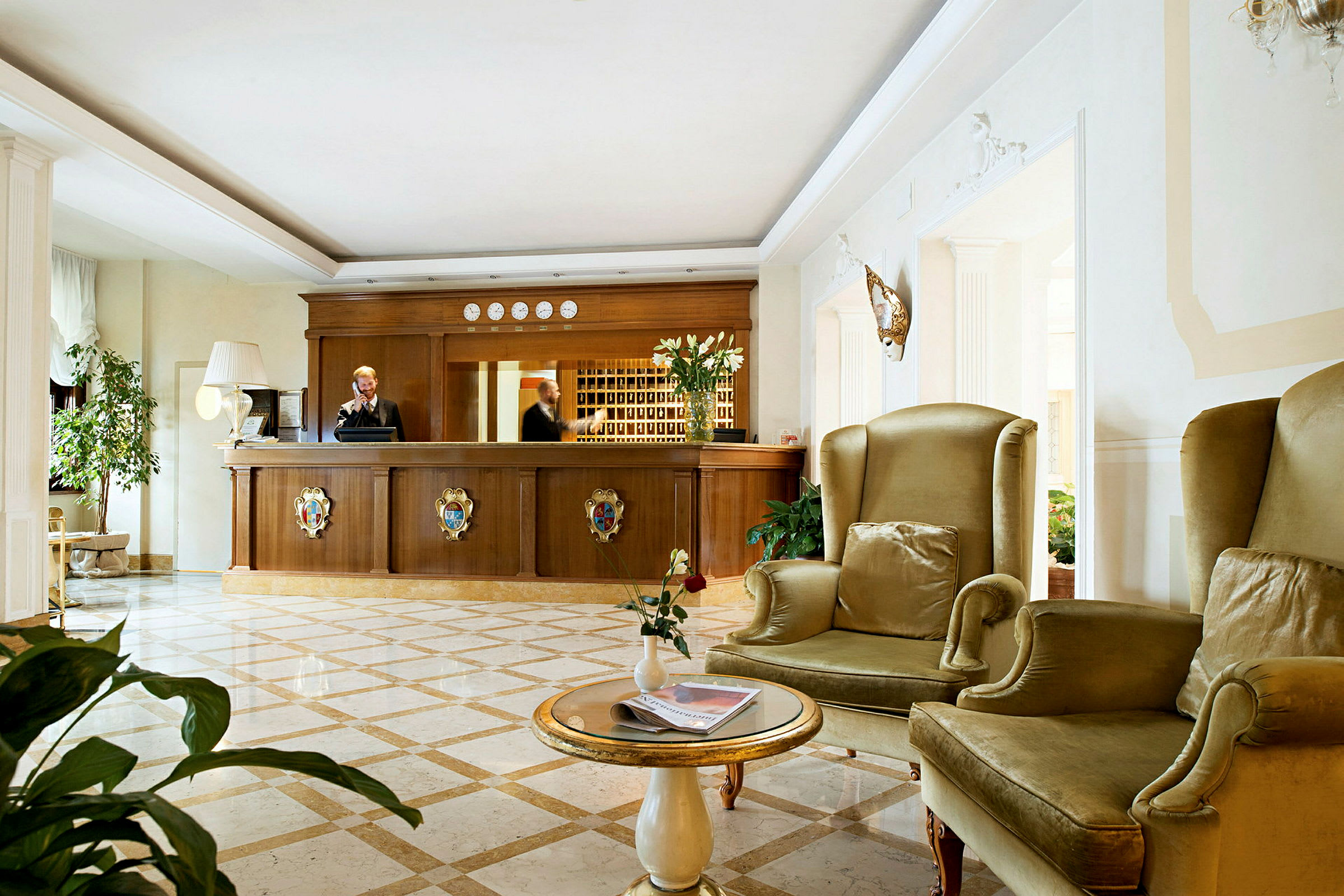 Ett hotellreceptionområde med en reception i trä och sittplatser med gröna fåtöljer. (AI-genererad text)
