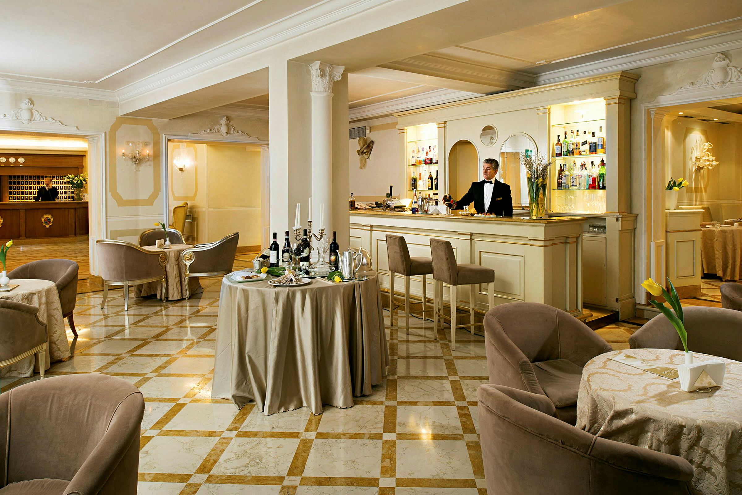 En elegant hotellbar med marmorgolv, små bord och bekväma stolar, samt en bartender vid disken. (AI-genererad text)