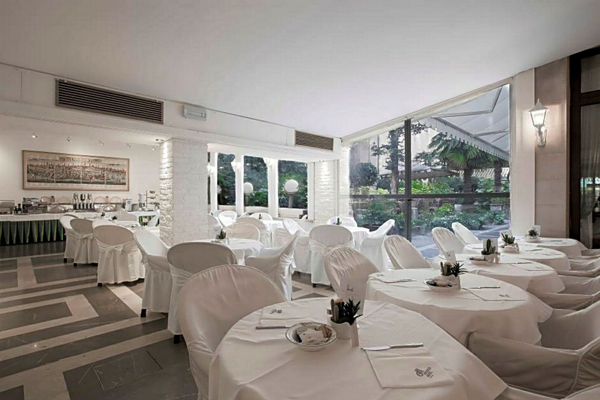 En restaurang med vita dukar och stolar, stora fönster och utsikt över en grönskande trädgård. (AI-genererad text)