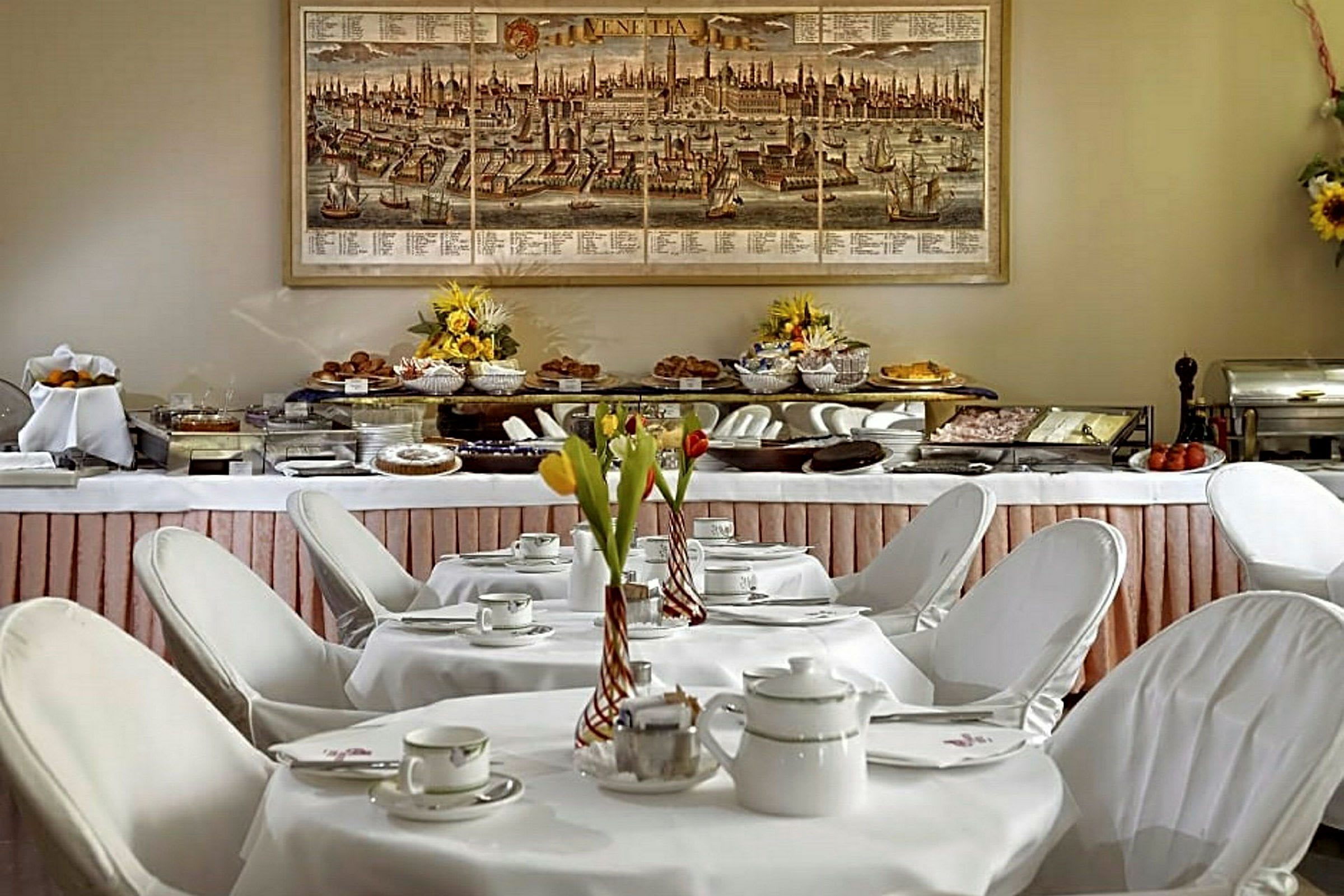 Ett frukostbord dukat med porslin och blomsterdekorationer framför en buffé fylld med maträtter. (AI-genererad text)