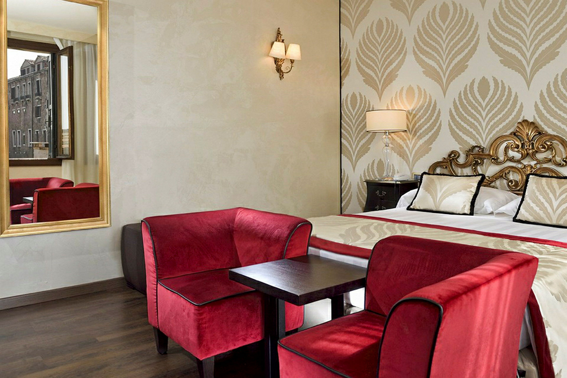 Ett elegant hotellrum med en dubbelsäng, röda fåtöljer och ett litet bord, samt ett fönster med utsikt. (AI-genererad text)
